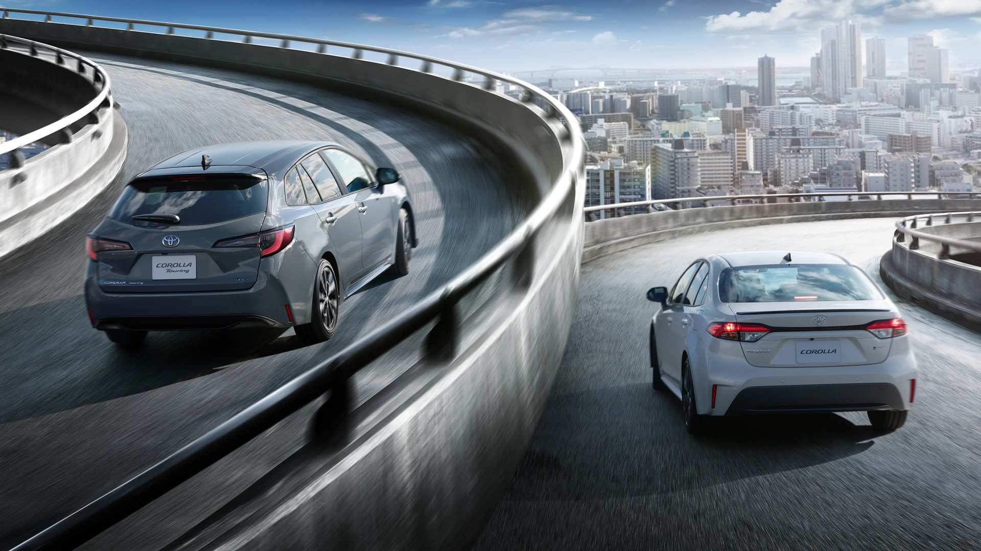 Two Toyota Corolla cars, one gray hatchback and one white sedan, driving on a curved elevated highway with a city skyline in the background.