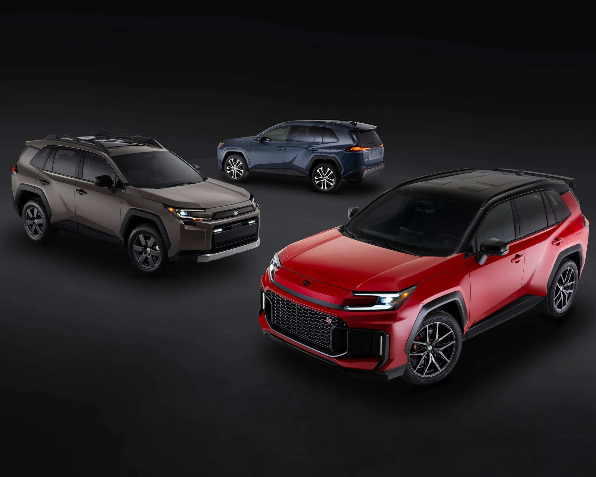 Three Toyota RAV4 SUVs in red, brown, and blue on a dark background.
