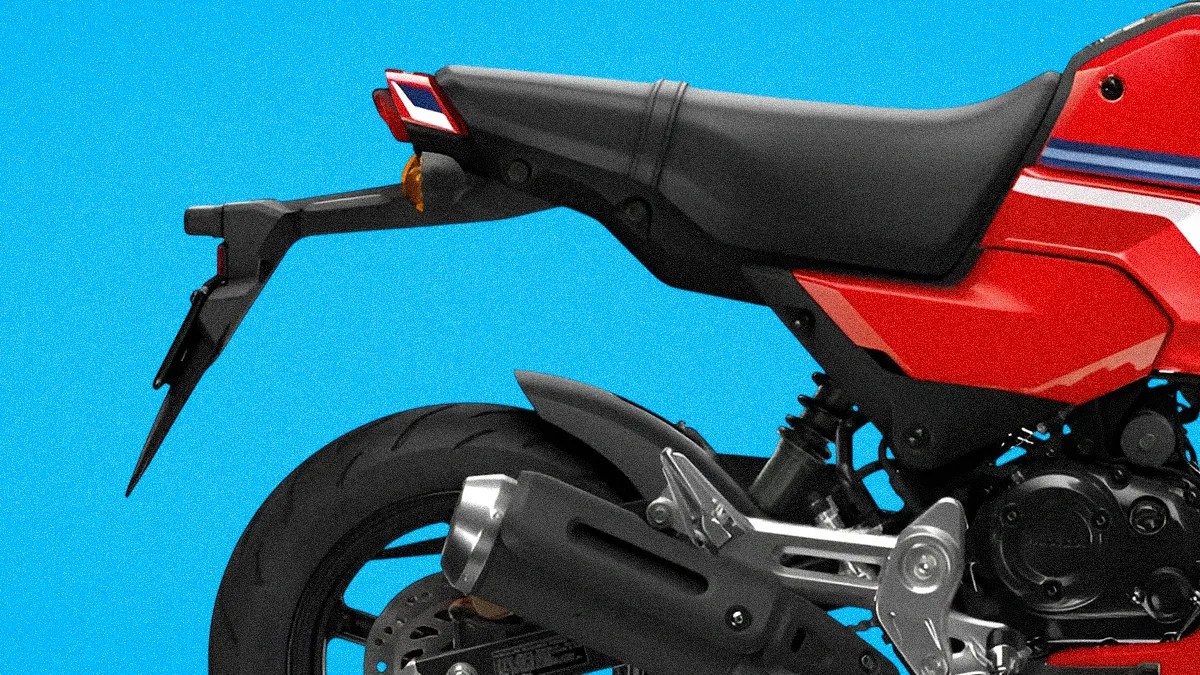 Rear section of a red motorcycle with black seat, exhaust pipe, and rear tire against a blue background.