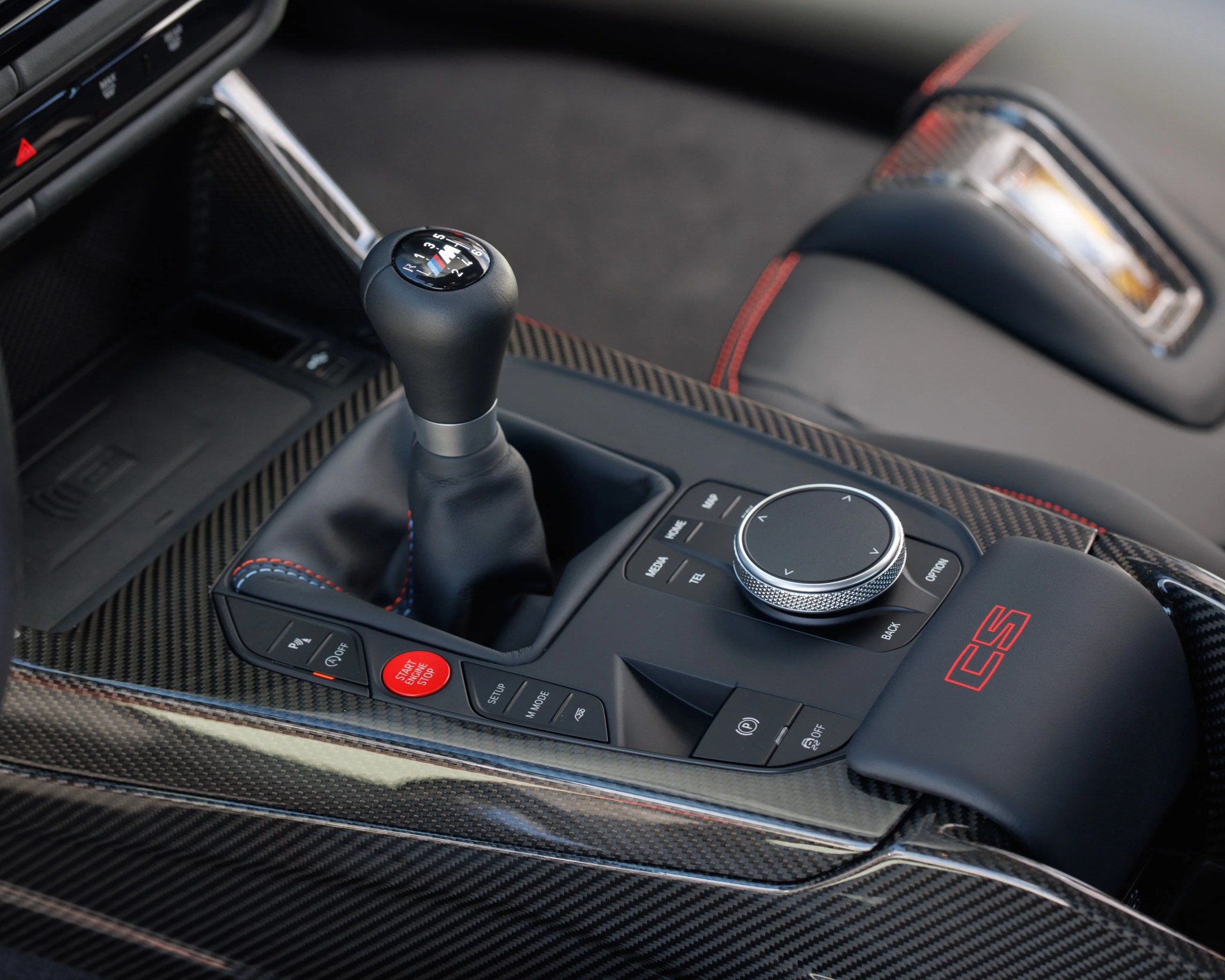 Black leather manual gear shift knob with BMW M logo on carbon fiber center console with red start engine button.