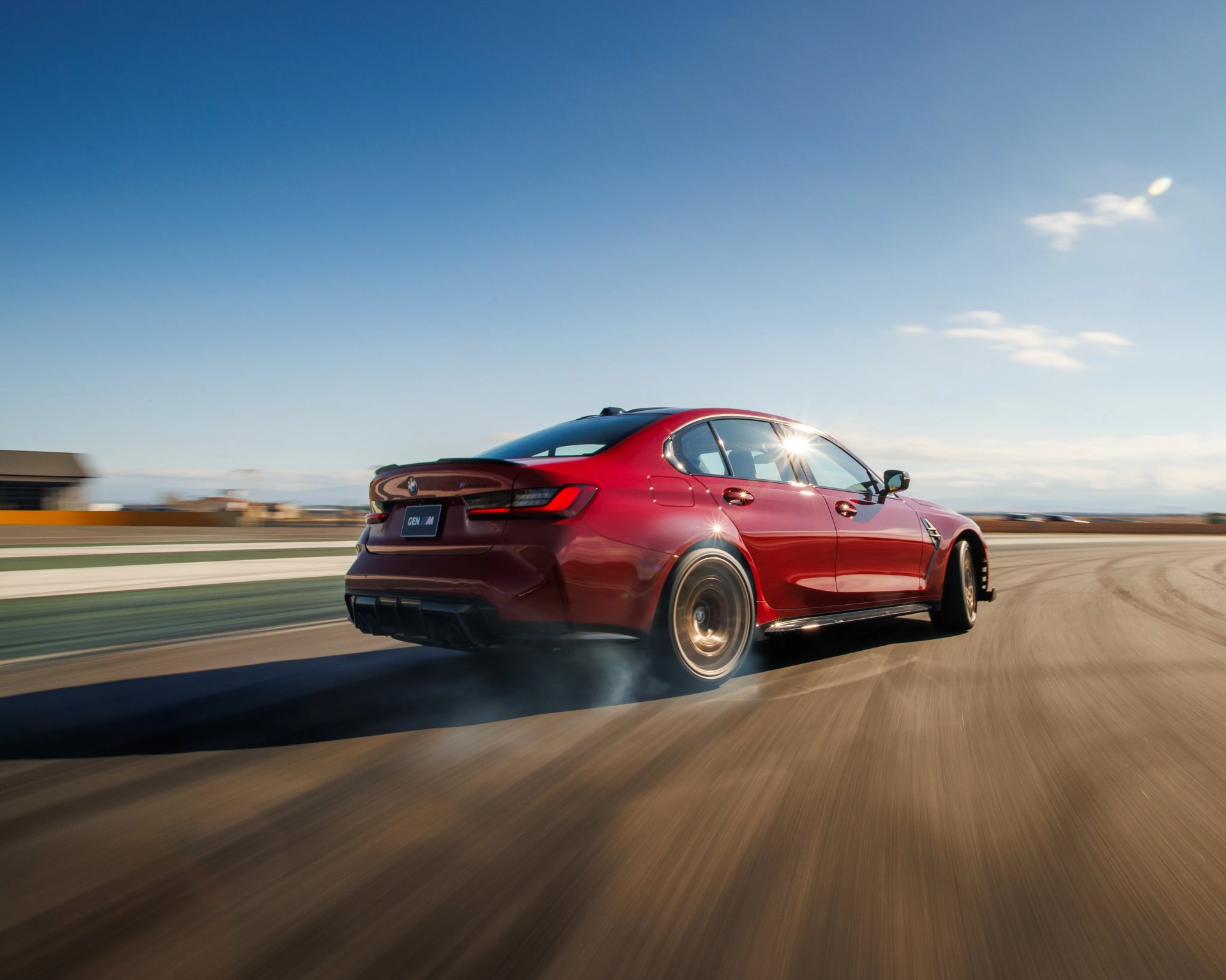 Red BMW sedan drifting on a race track under a clear blue sky.