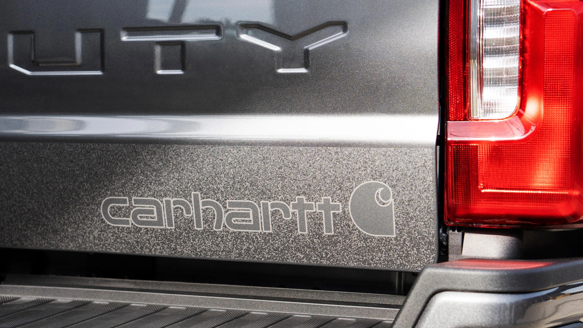 Close-up of a gray truck tailgate with embossed "UTY" and "carhartt" logo next to a red taillight.