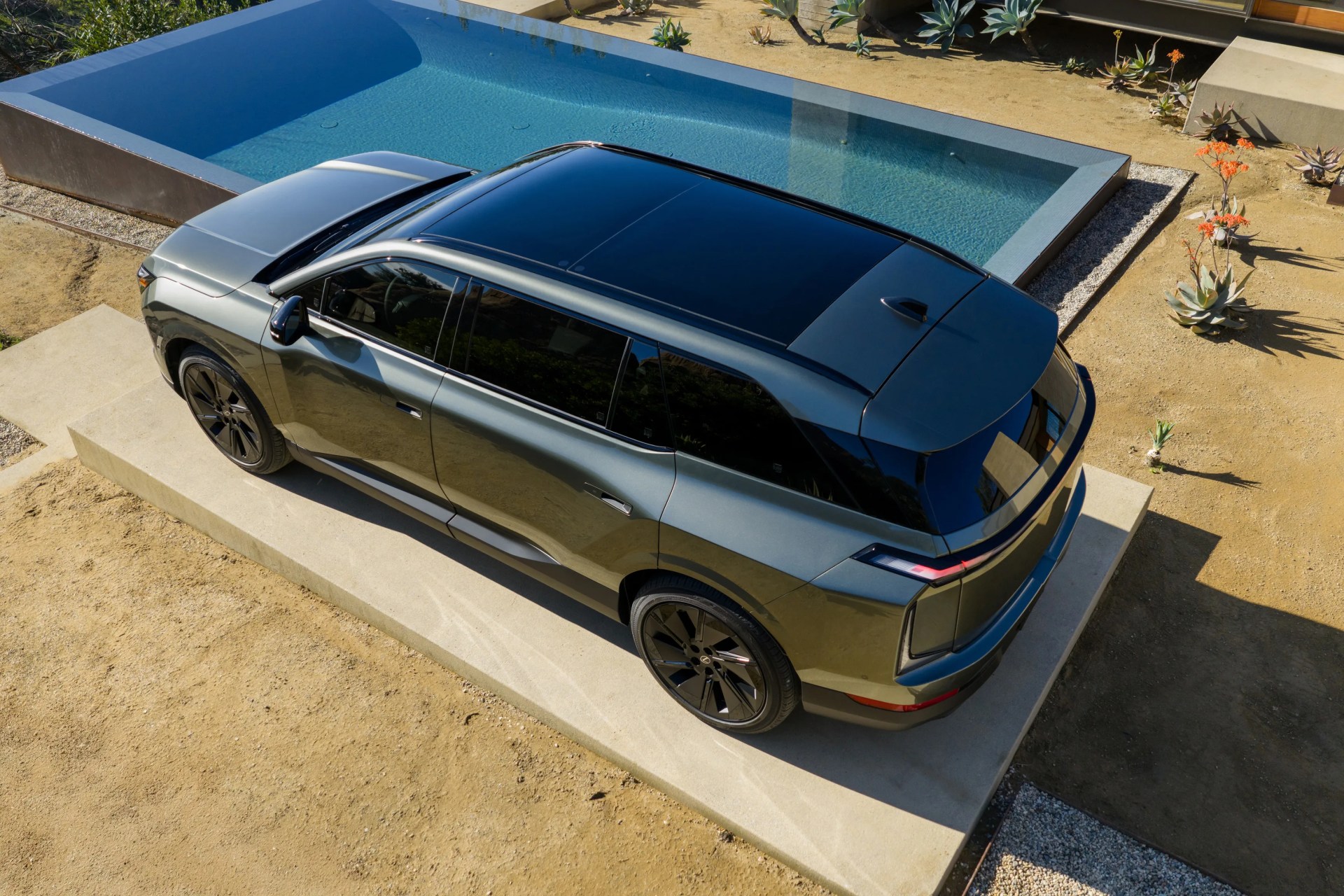 Metallic gray SUV with black roof and wheels parked on a concrete platform near a rectangular pool.