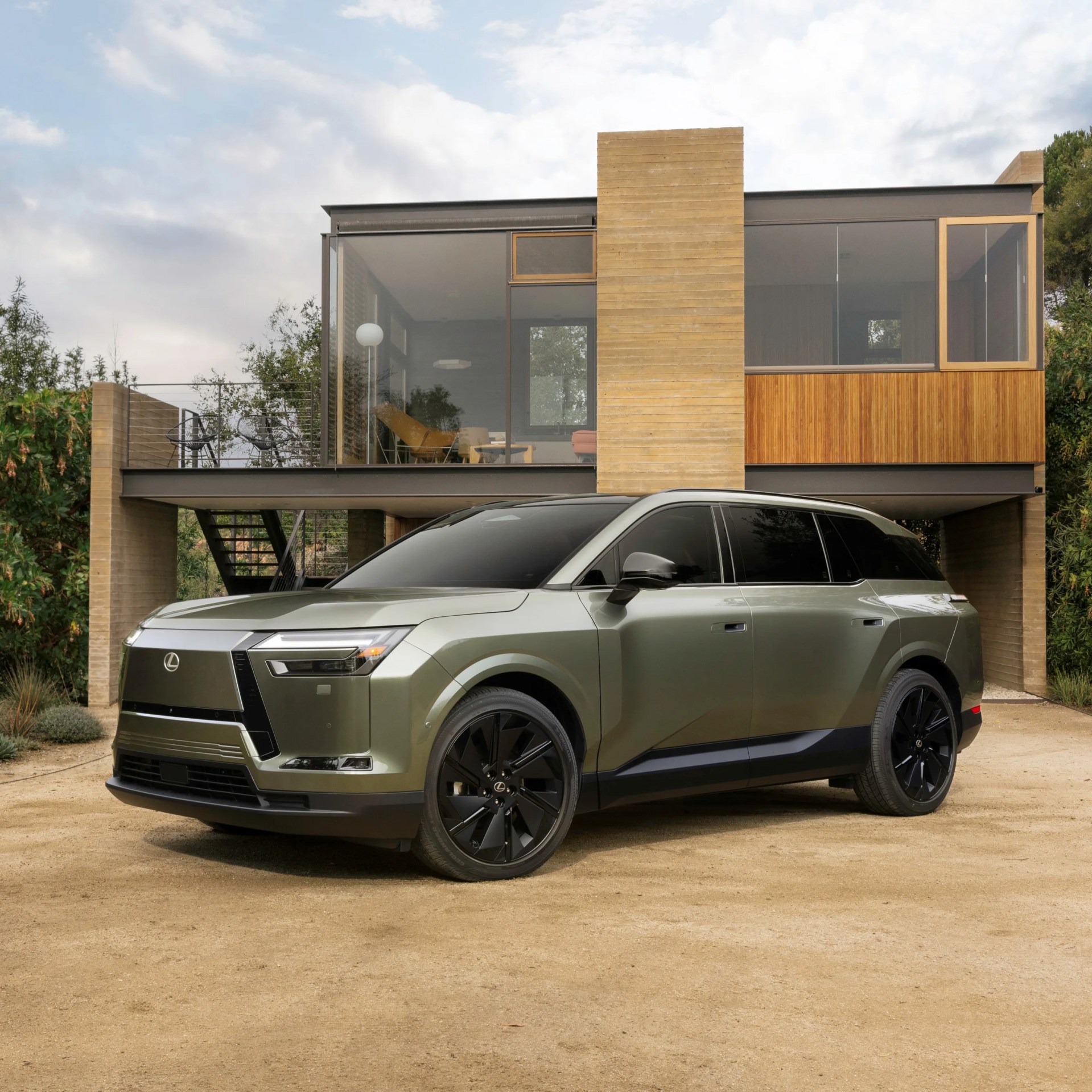 Green Lexus SUV with black wheels parked in front of a modern house with large glass windows.