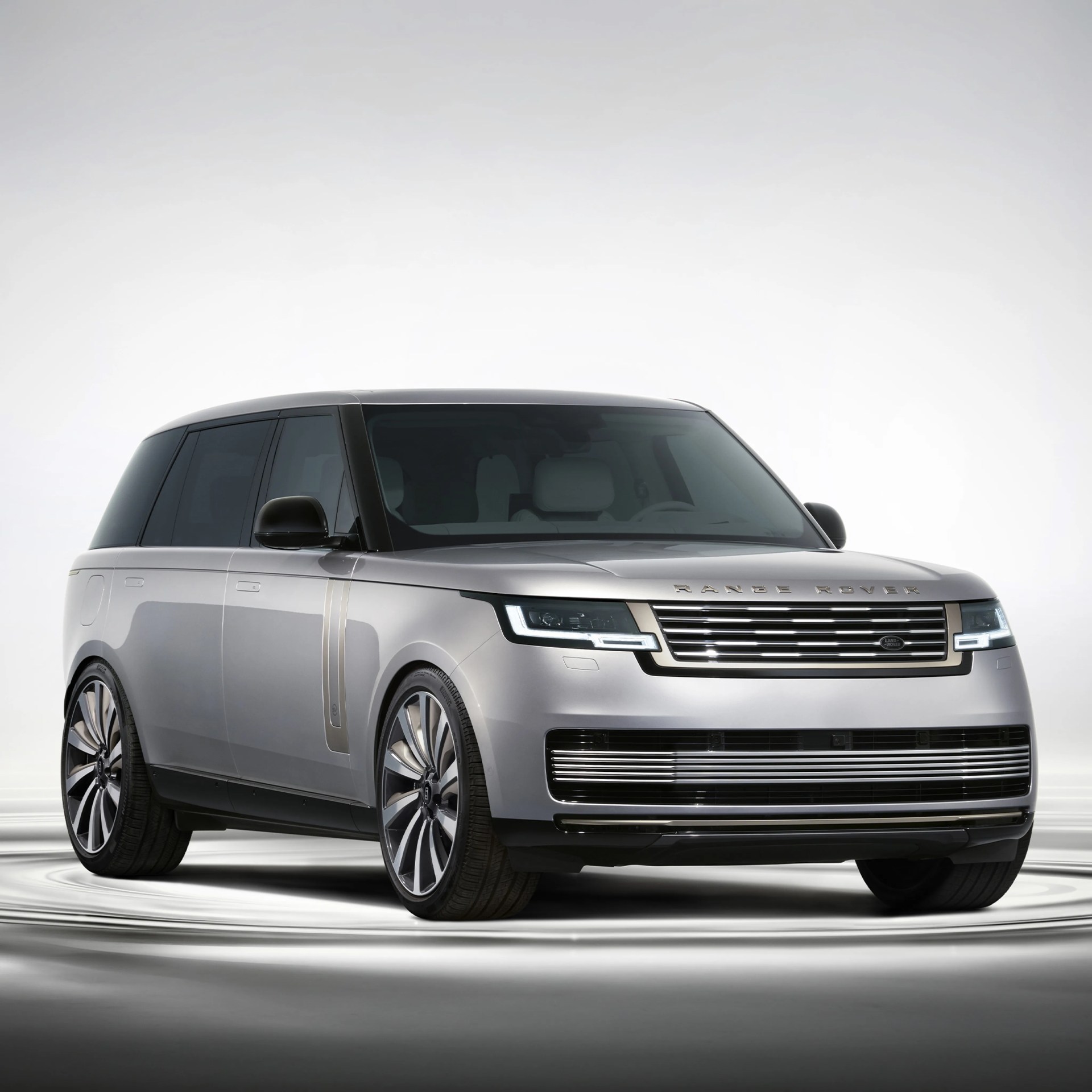 Silver Range Rover SUV with black tinted windows and modern LED headlights on a reflective surface.
