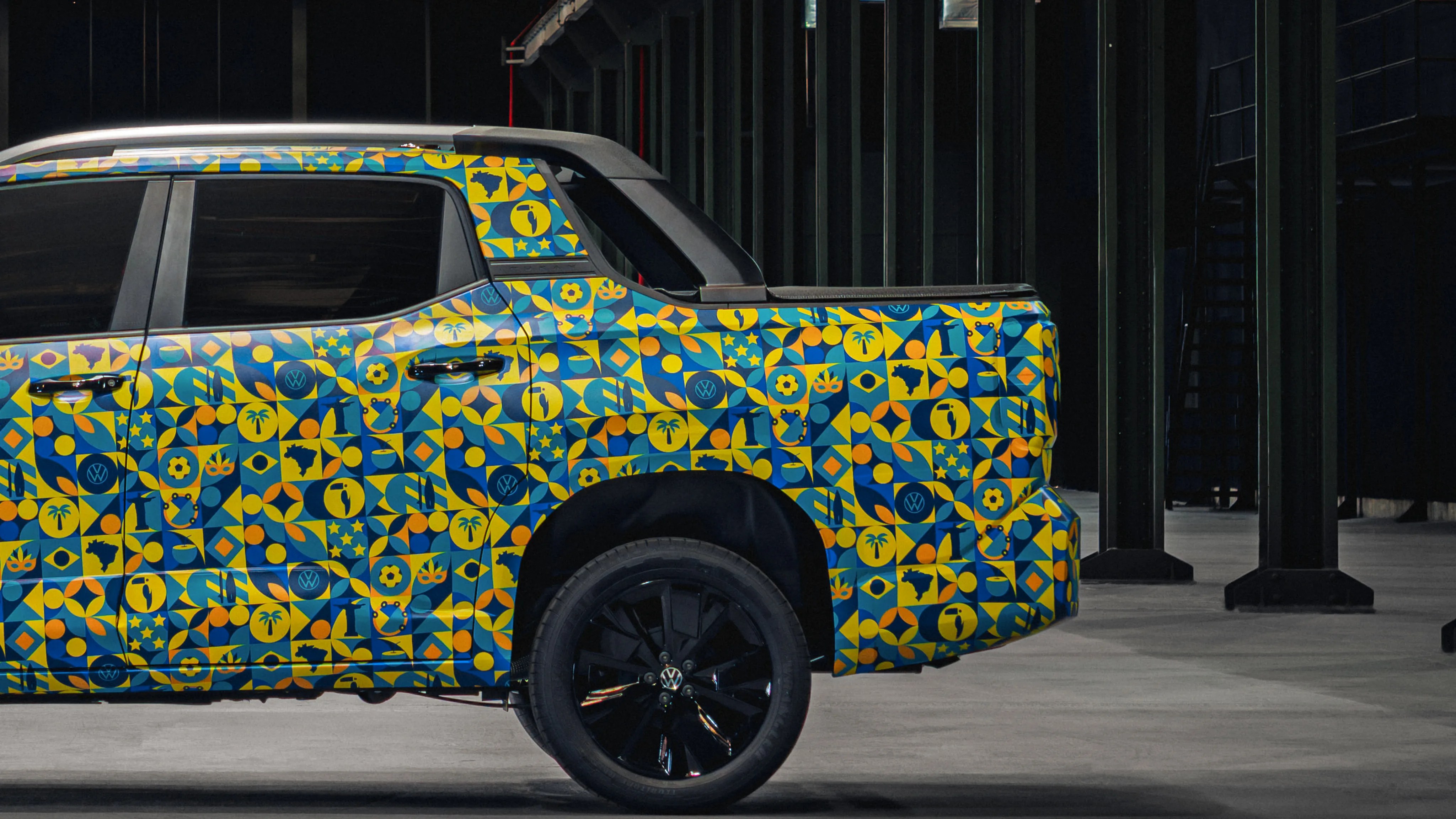 Side view of a pickup truck with a colorful geometric pattern wrap featuring blue, yellow, and orange shapes and black wheels.