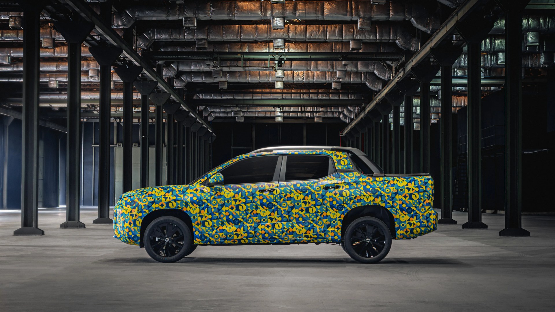 Side view of a pickup truck with a blue and yellow geometric patterned wrap and black wheels in an industrial warehouse.
