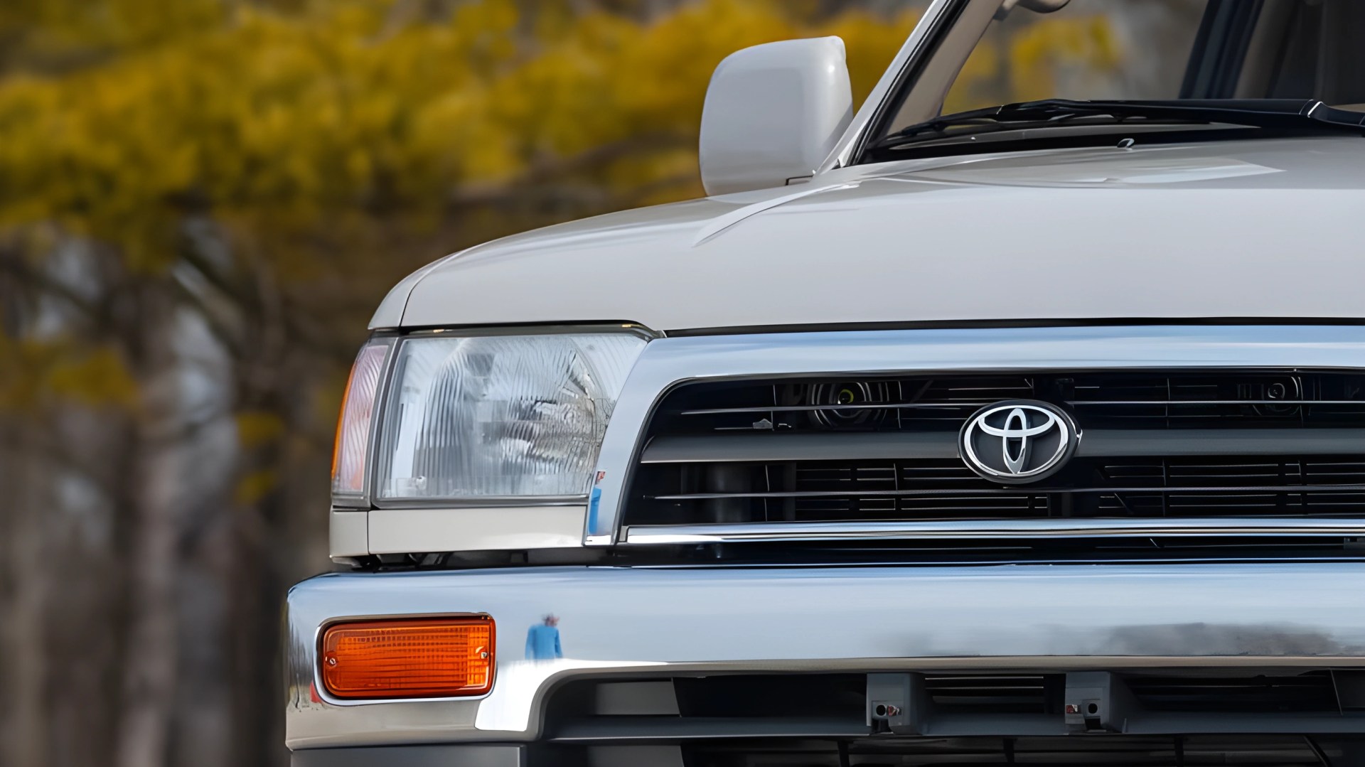 Close-up of a white Toyota vehicle front grille with logo, headlight, and amber turn signal light.
