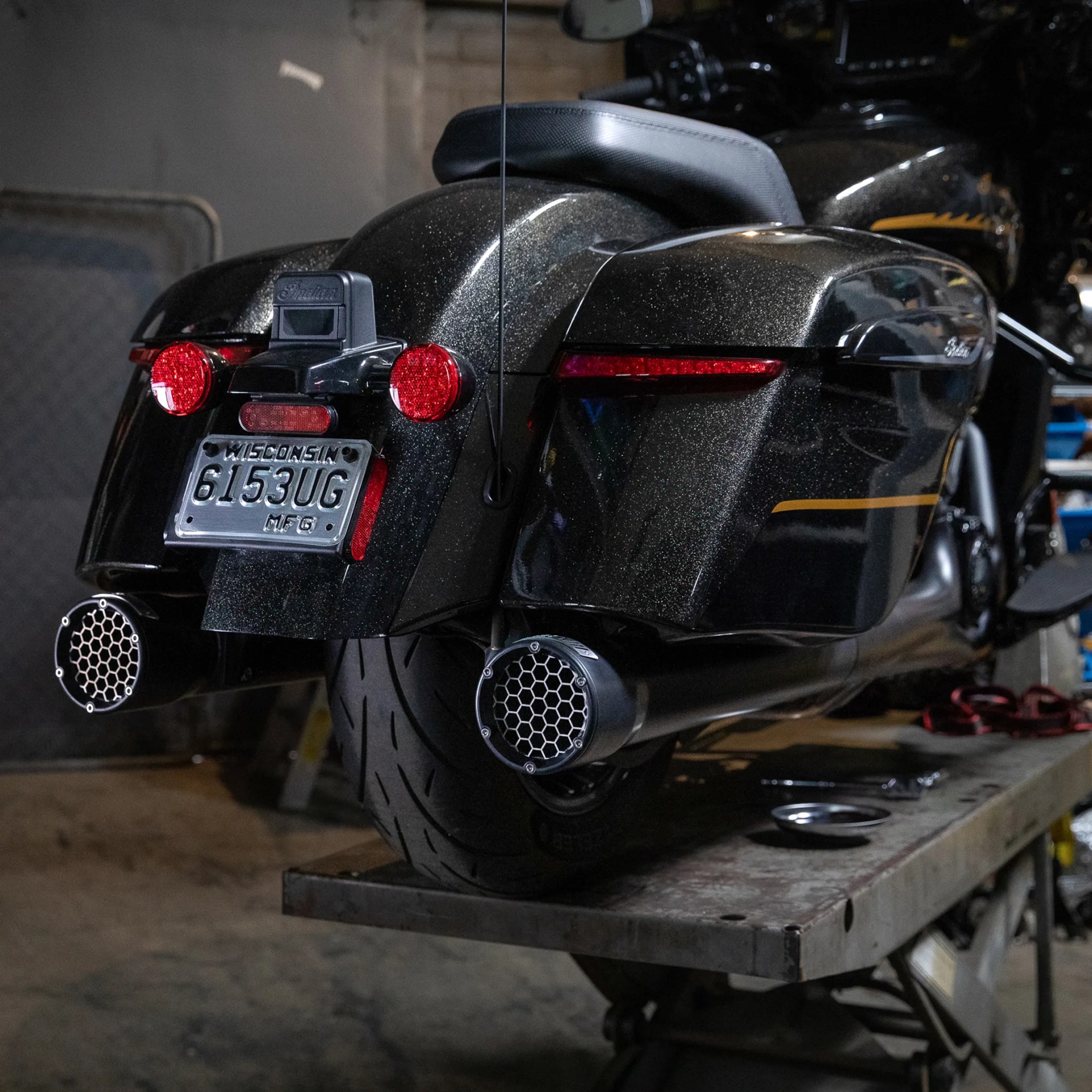 Black metallic Indian motorcycle rear with saddlebags, dual exhausts, and Wisconsin license plate on a lift.