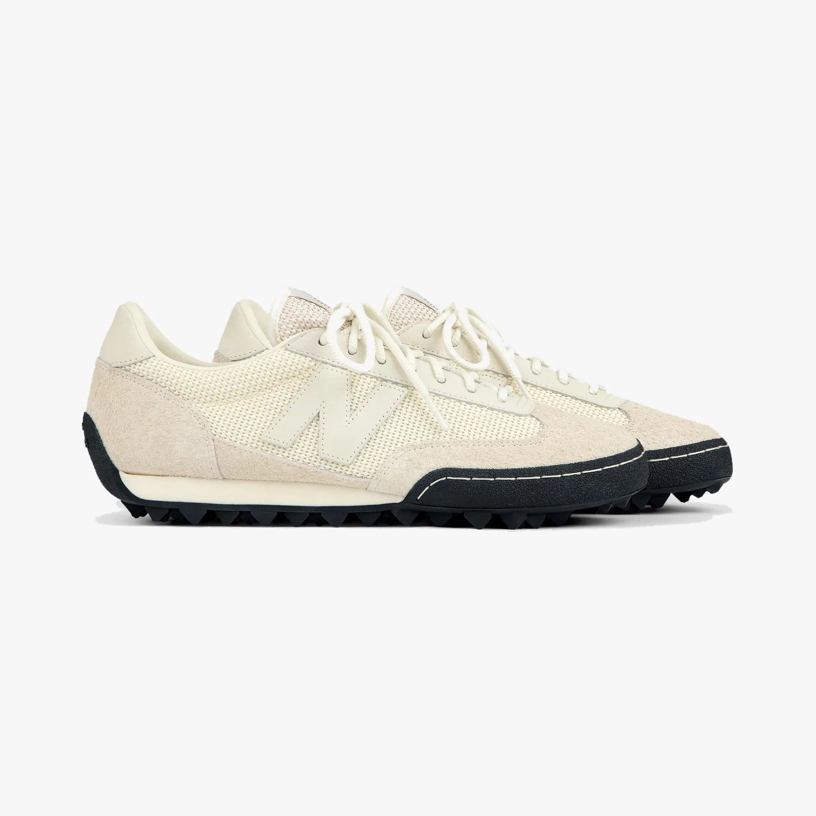 Pair of off-white New Balance sneakers with suede and mesh upper and black textured soles.