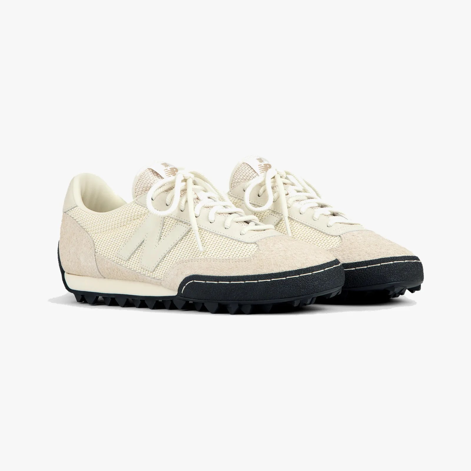 Pair of off-white New Balance sneakers with suede and mesh upper and black textured sole.