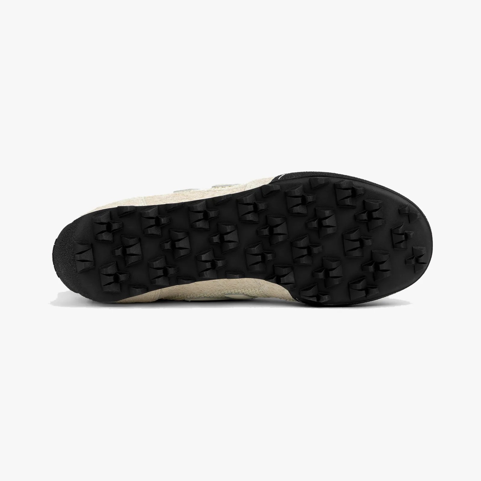 Black rubber outsole with triangular lugs on a beige shoe sole.