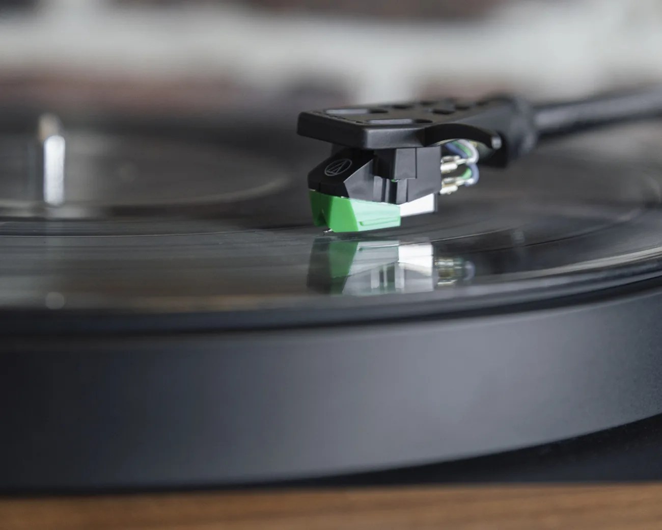 Close-up of a black and green cartridge stylus on a spinning vinyl record on a turntable.