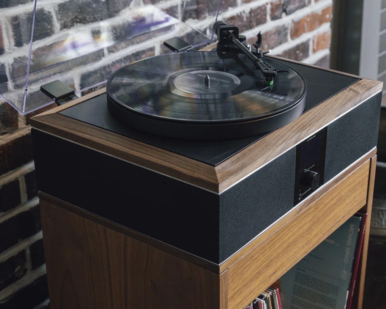 Turntable with a black vinyl record on a wooden cabinet against a brick wall.