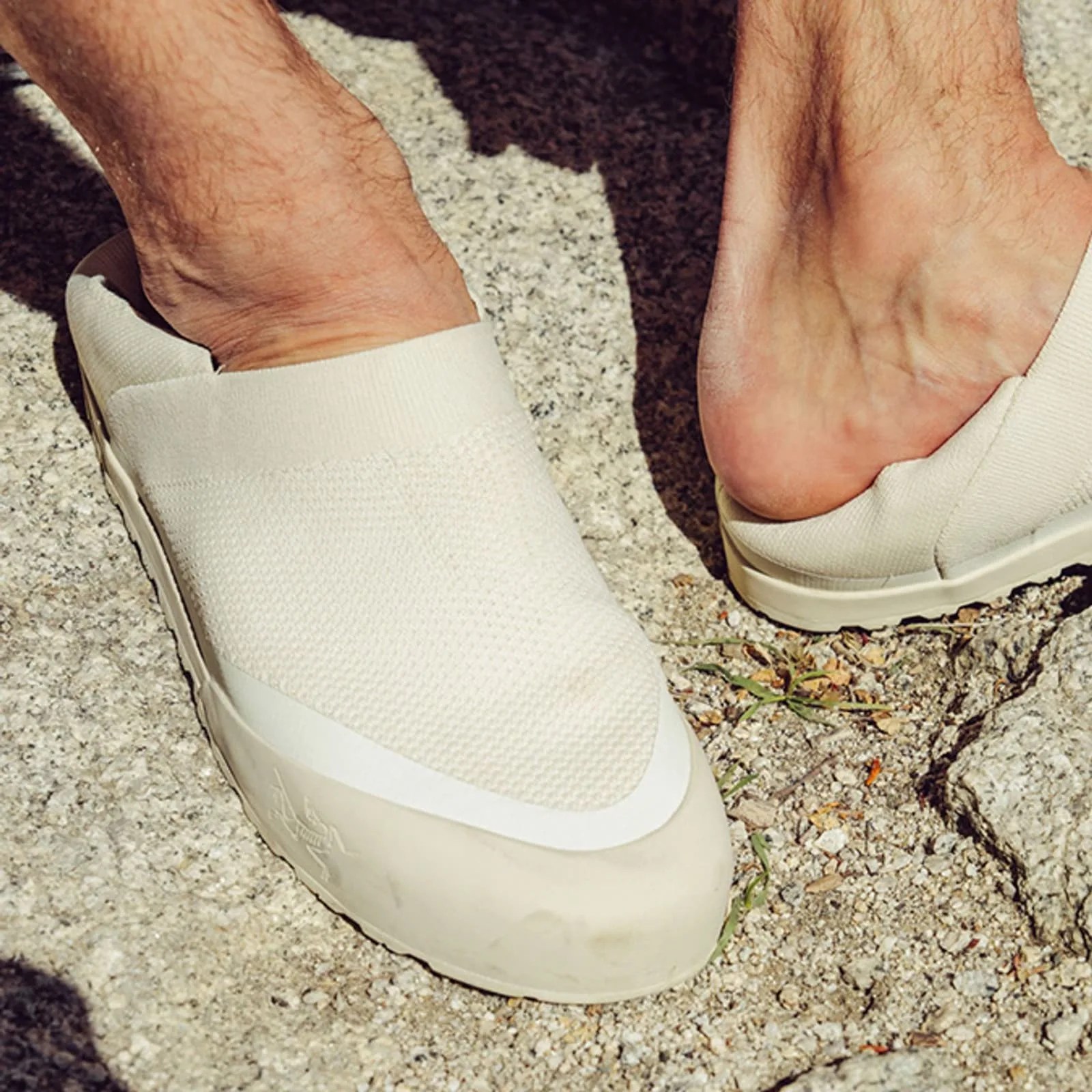 Beige slip-on shoes with textured fabric uppers and rubber soles worn on feet on a gravel surface.