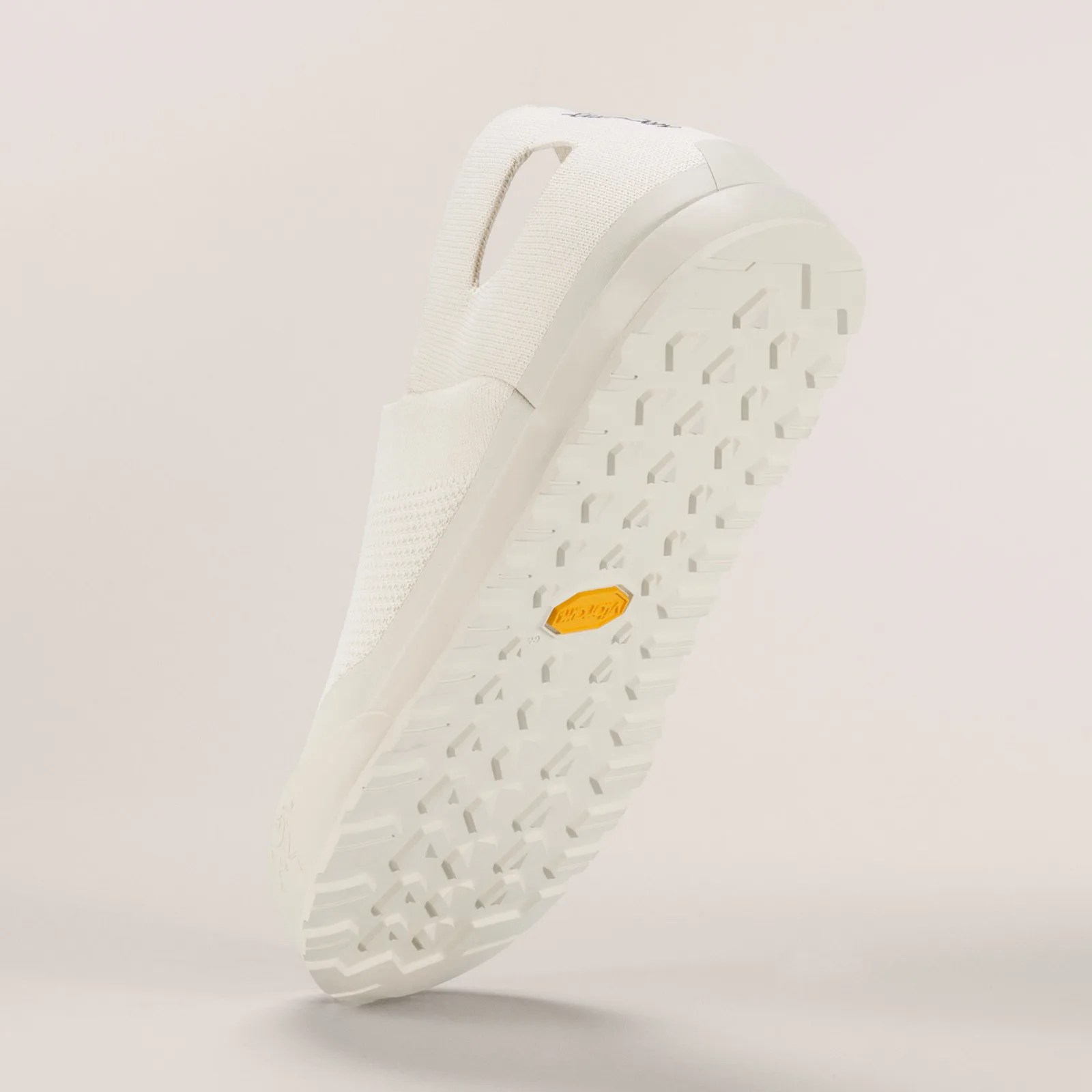 Off-white knit slip-on shoe with textured sole and yellow Vibram logo on the bottom.