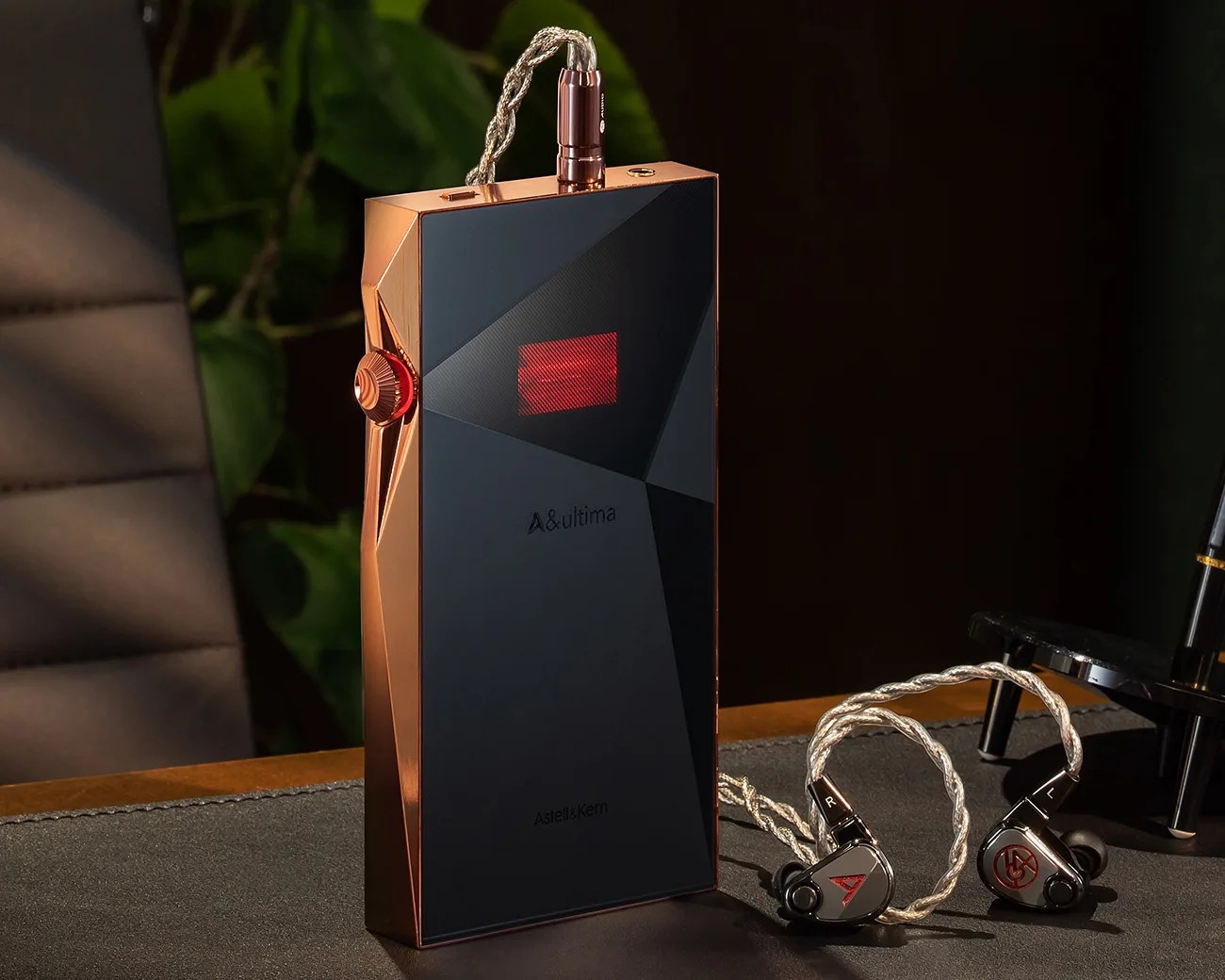 Copper and black Astell&Kern portable music player with attached silver braided cable and black earphones on a dark surface.