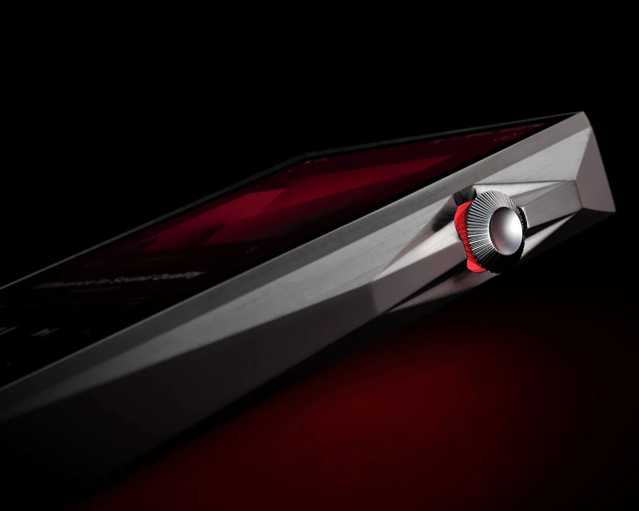 Close-up of a metallic device with a faceted edge and a textured silver crown with red accents on a dark background.