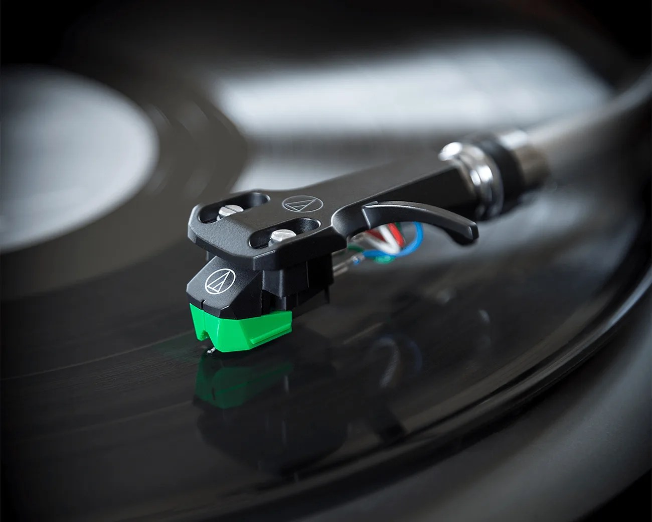 Close-up of a black and green Audio-Technica turntable cartridge and stylus on a spinning vinyl record.