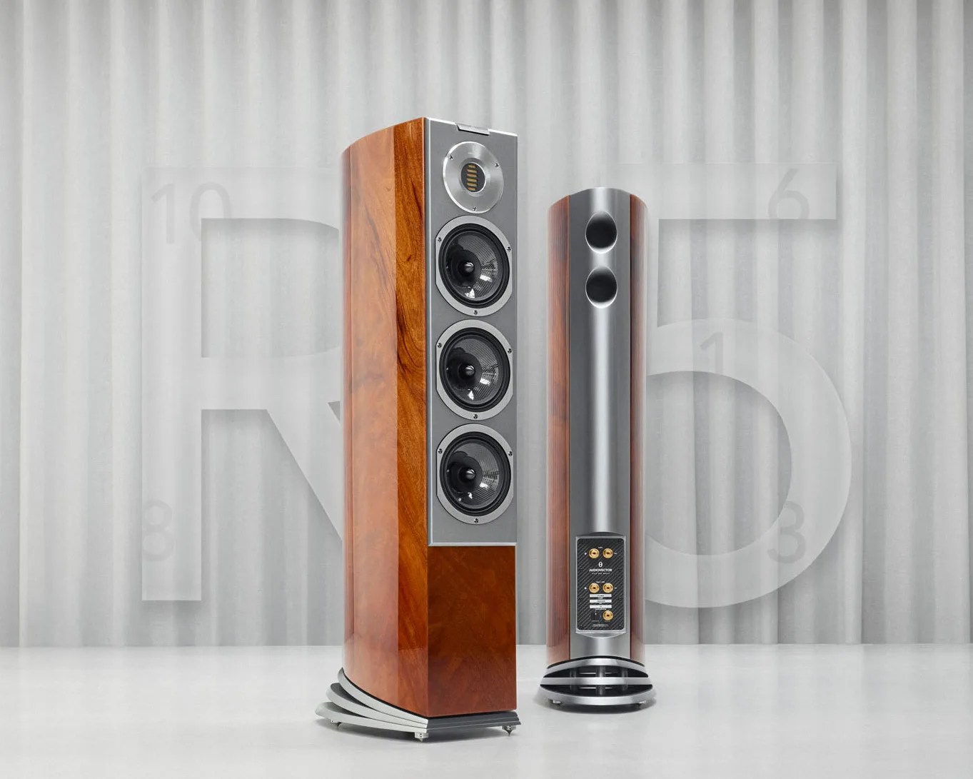 Pair of tall floor-standing speakers with wood veneer sides, silver front panels, and multiple drivers, shown from front and back.