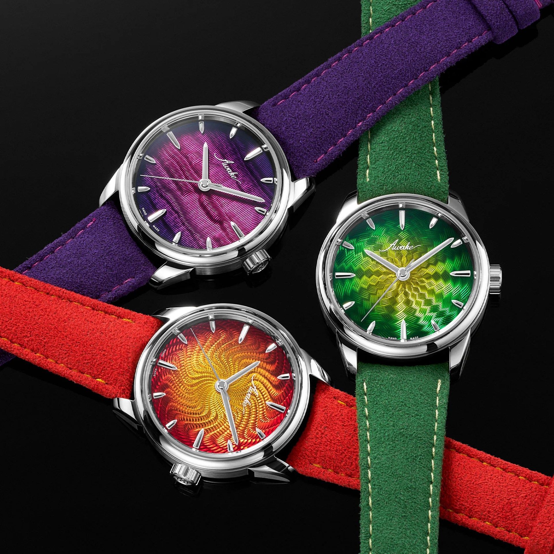 Three wristwatches with textured gradient dials in purple, green, and red, each with suede straps in purple, green, and red.