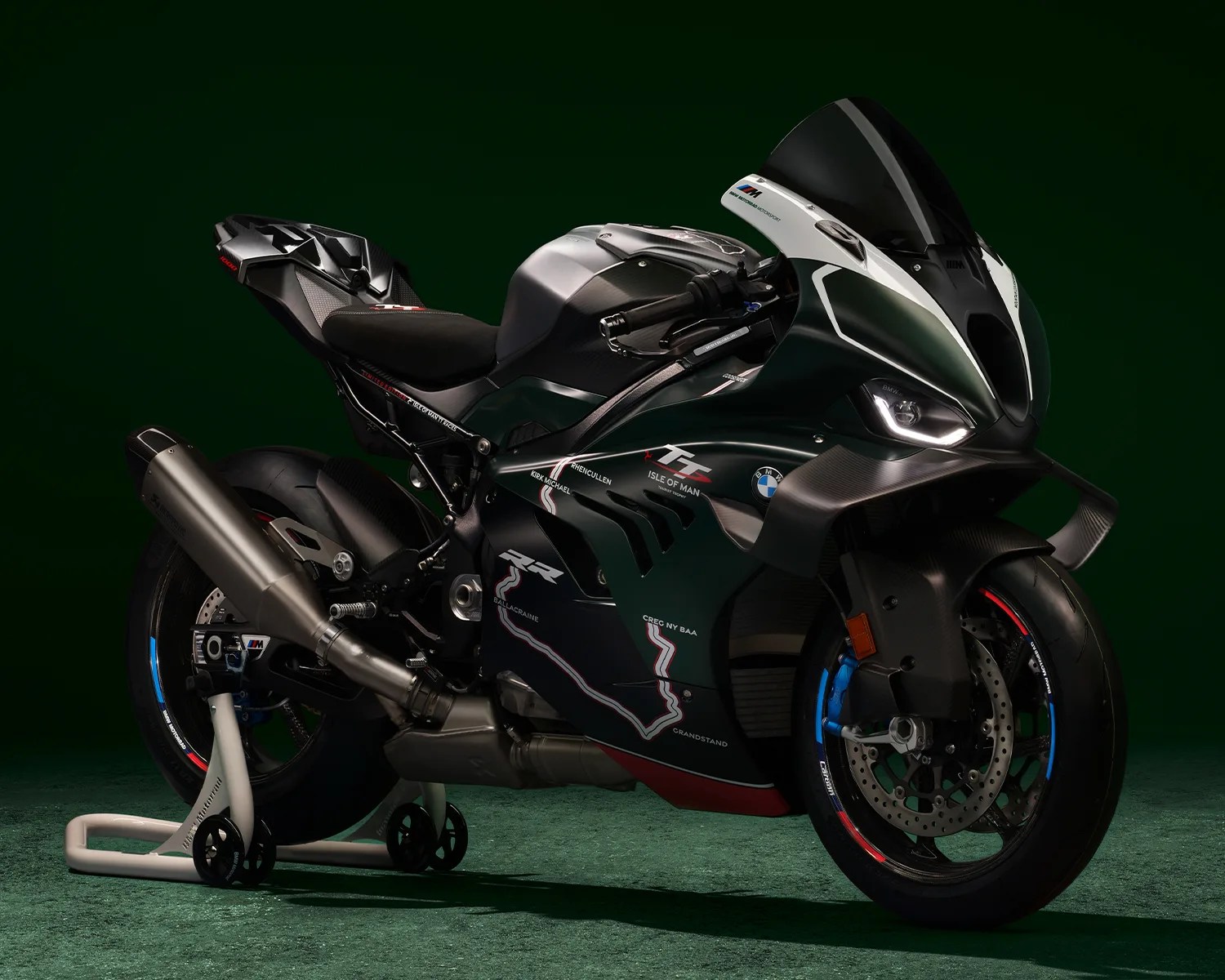 Dark green and black BMW sport motorcycle with Isle of Man TT race graphics on a green carpeted floor against a dark green background.