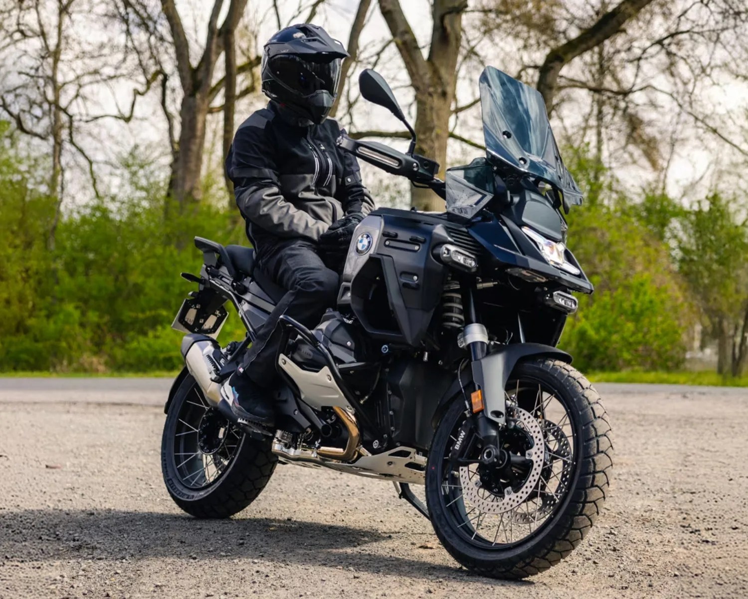 Black BMW adventure motorcycle with rider in black gear and helmet on a gravel road.