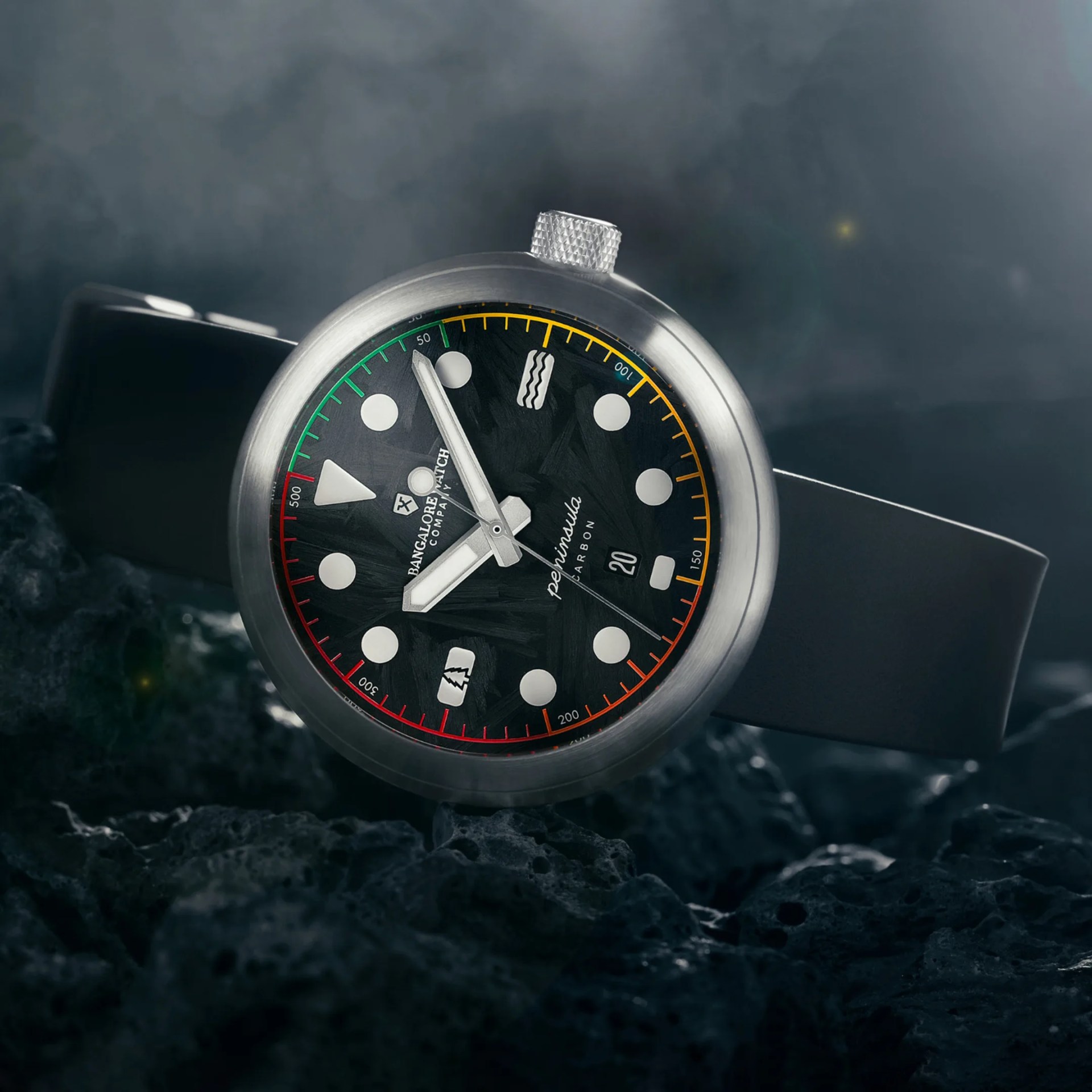Close-up of a black dial wristwatch with multicolored markers and a brushed metal case on a dark textured surface.