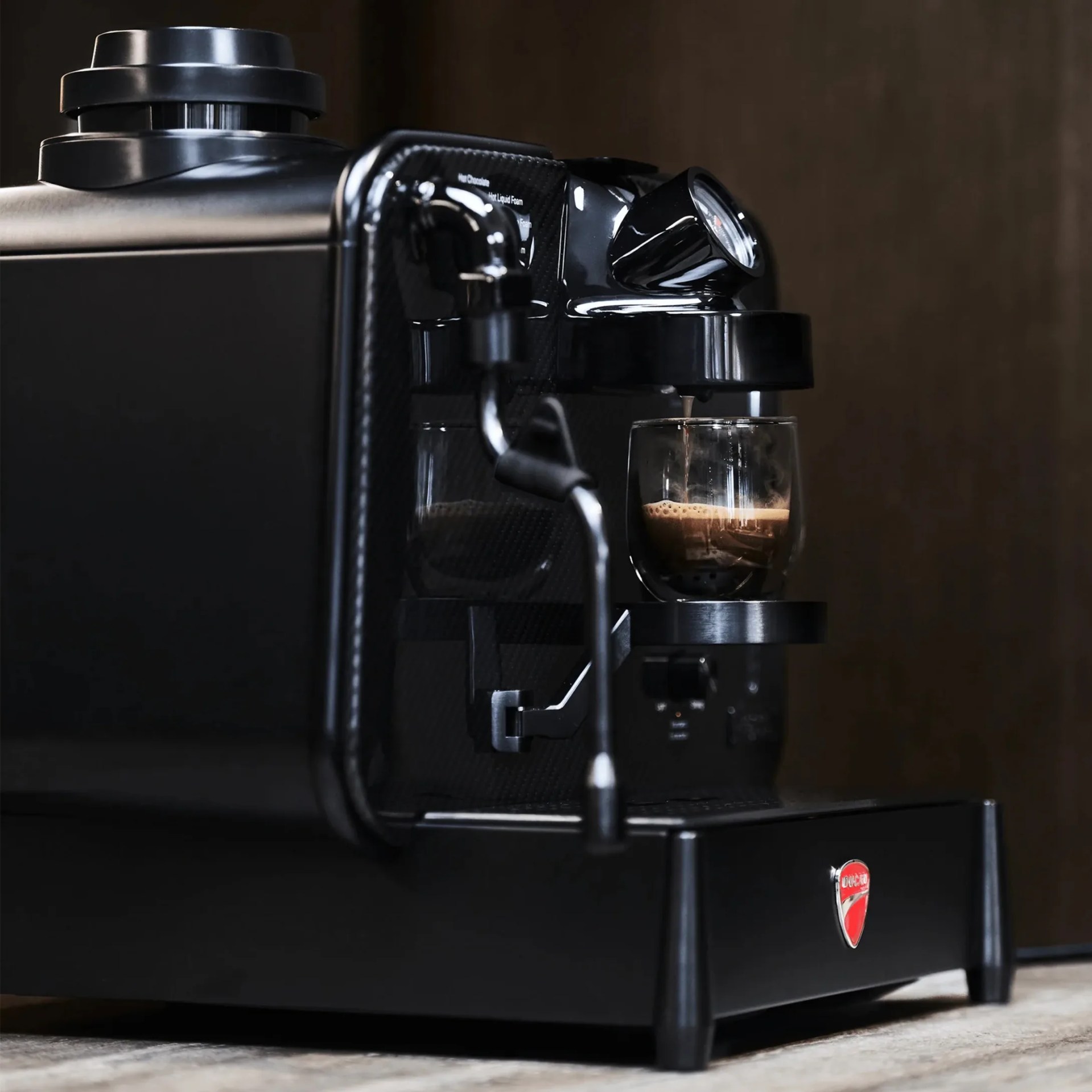 Black Ducati espresso machine with a glass cup brewing coffee on a wooden surface.