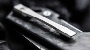 Close-up of a silver metal clip attached to a textured dark surface, likely part of a folding knife.