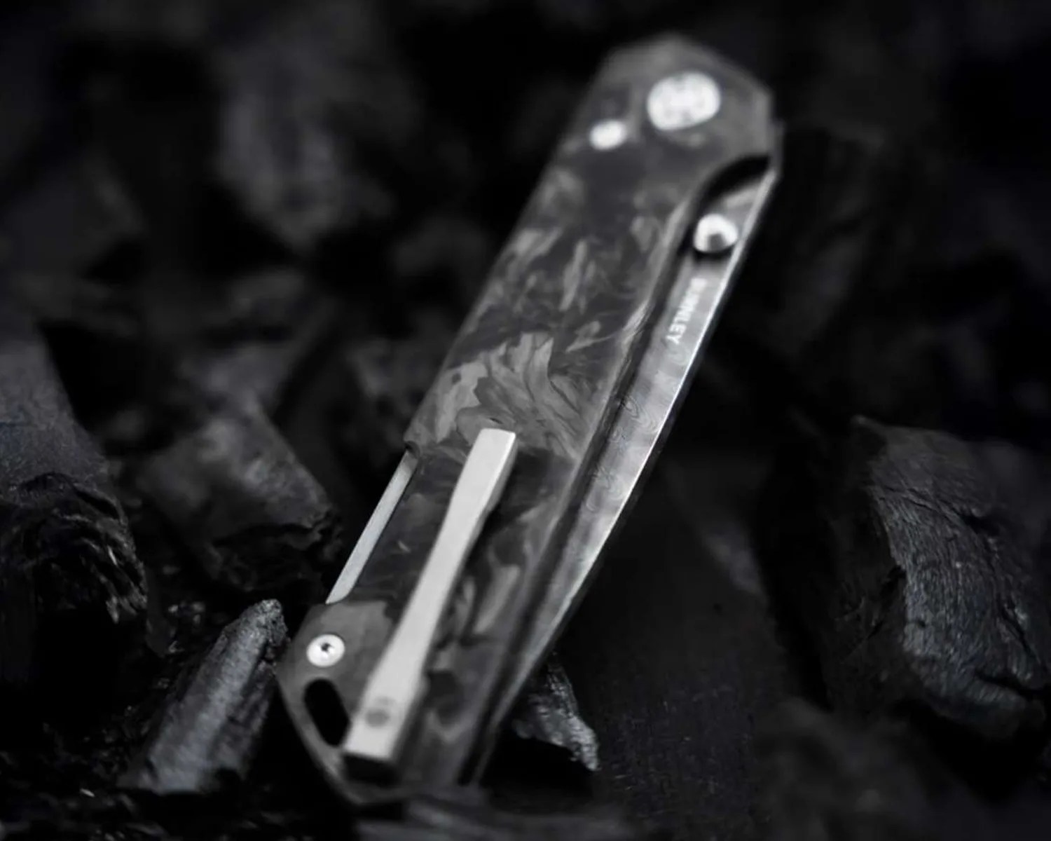 Folded black and gray marbled pocket knife with metal clip on a dark textured surface.