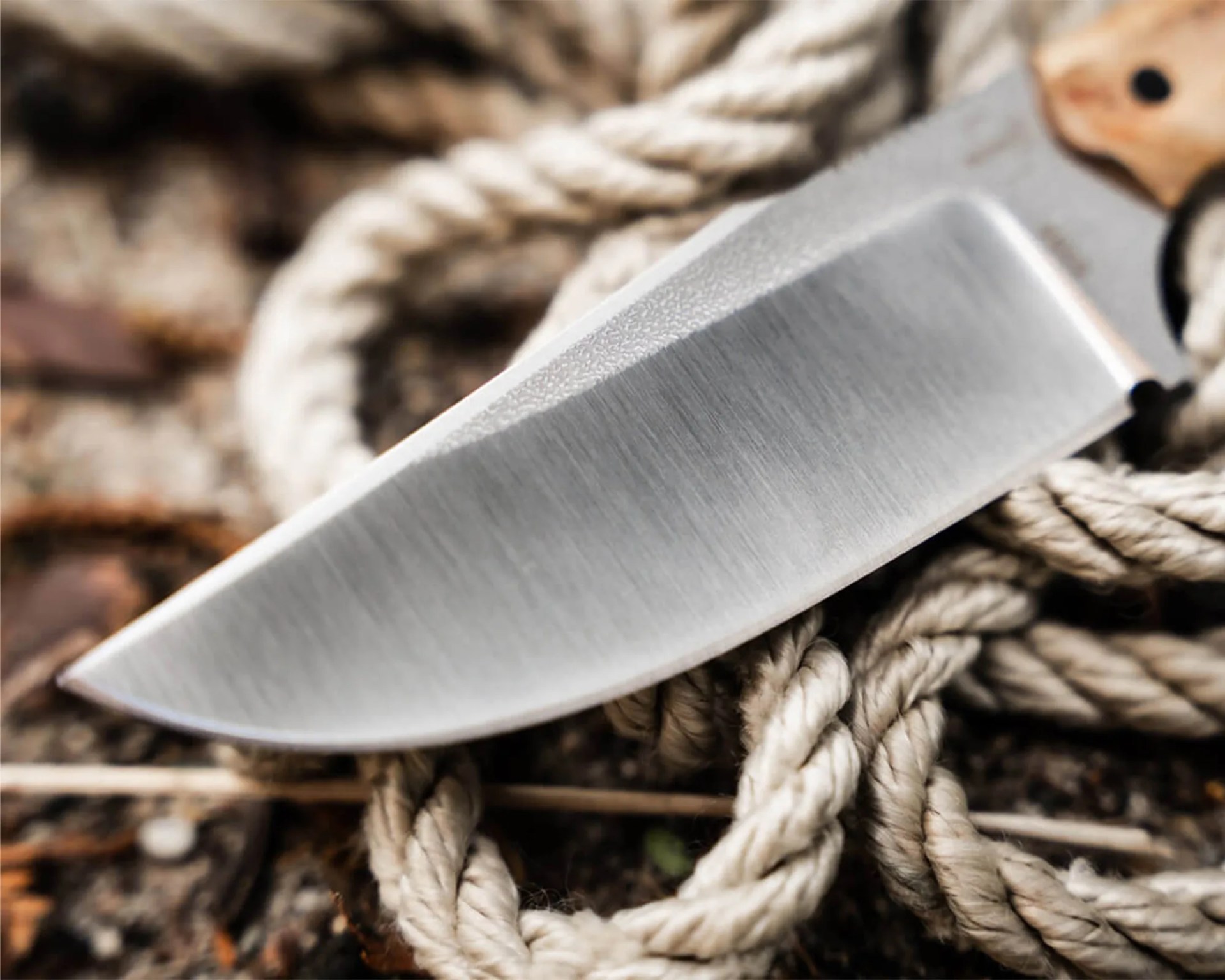 Close-up of a sharp stainless steel knife blade resting on coiled beige rope.