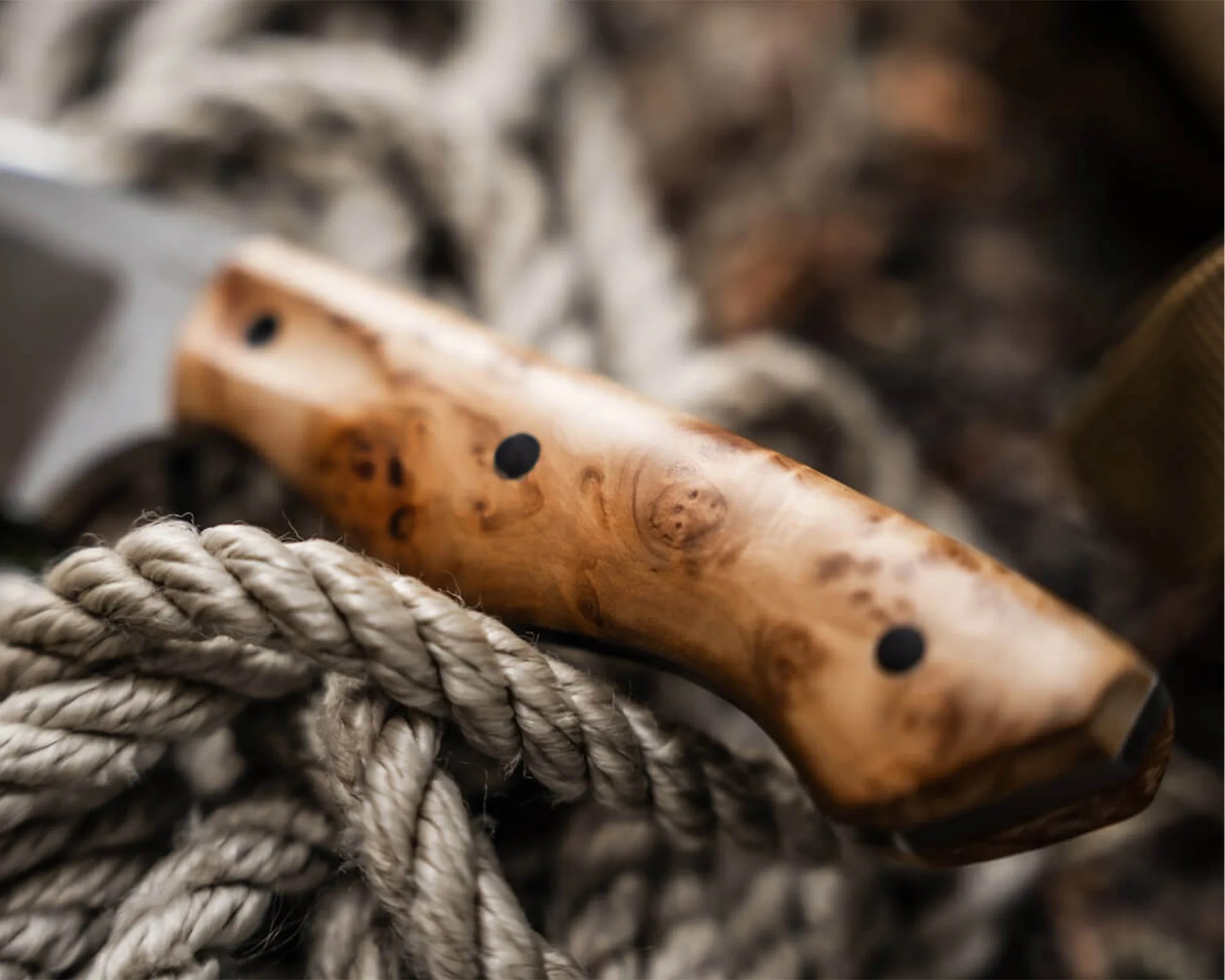 Close-up of a wooden handle with black dots resting on thick, twisted beige rope.