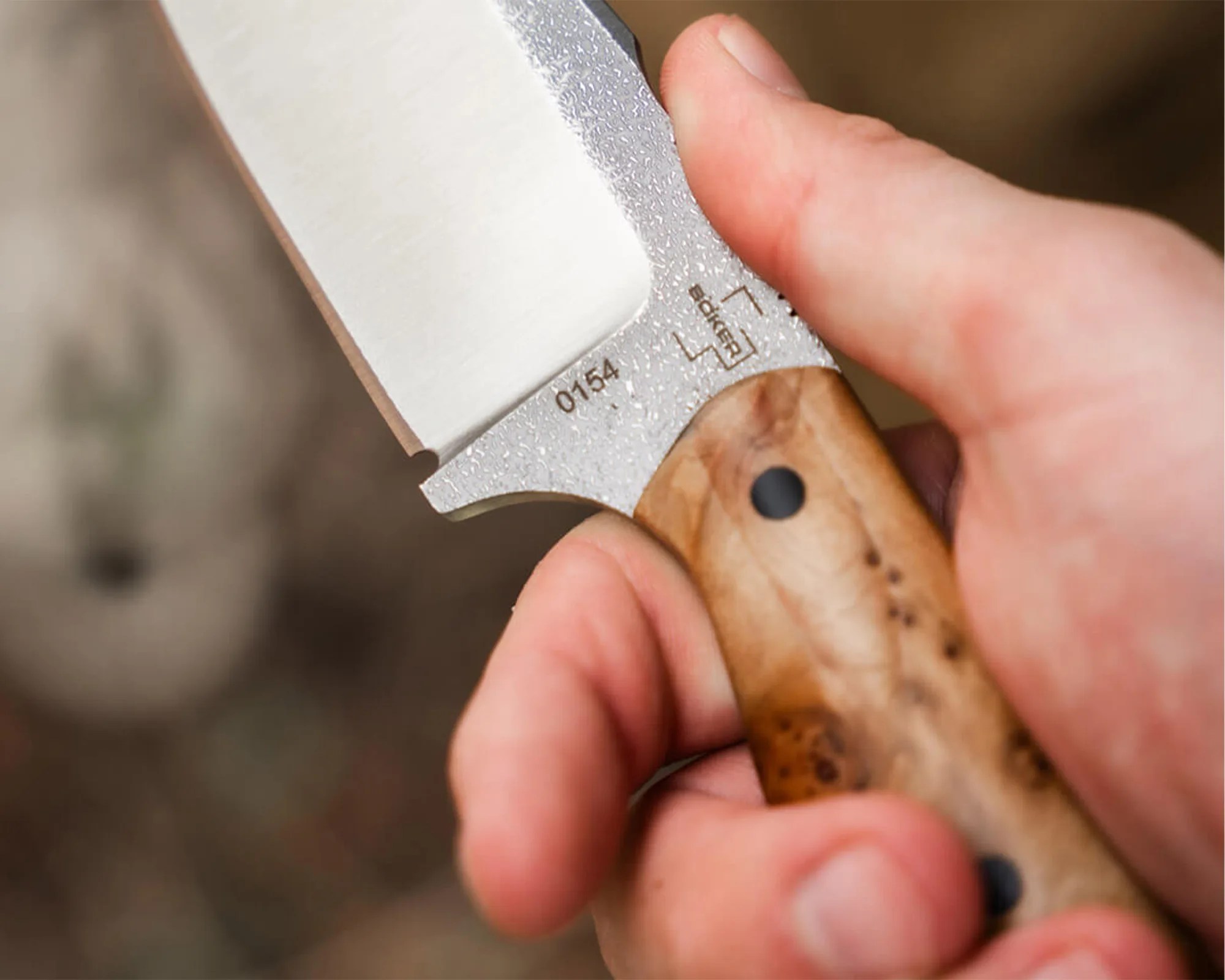 Hand holding a knife with a textured metal blade and a wooden handle with a black rivet.