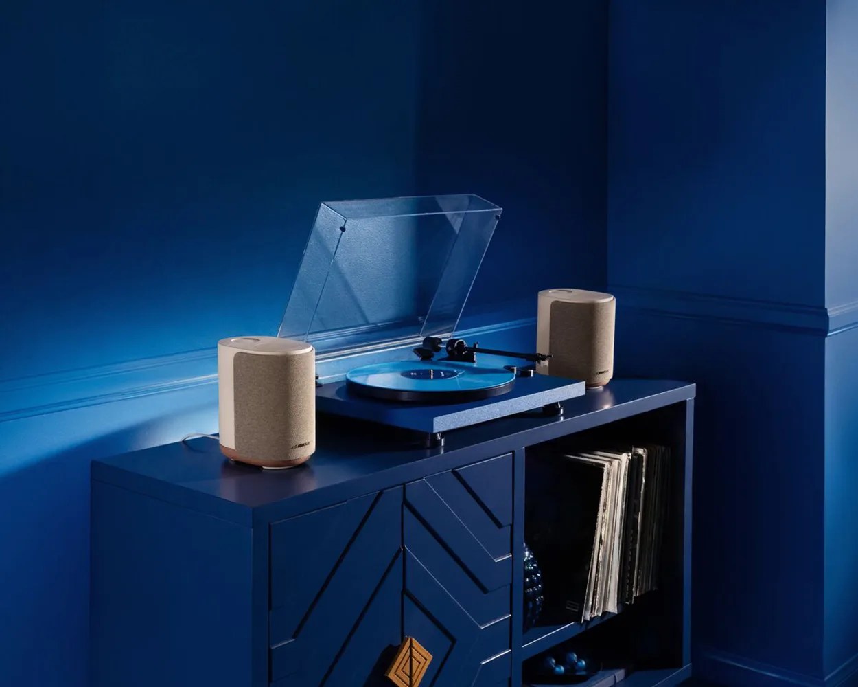 Blue turntable with transparent dust cover and beige speakers on a blue cabinet with vinyl records.