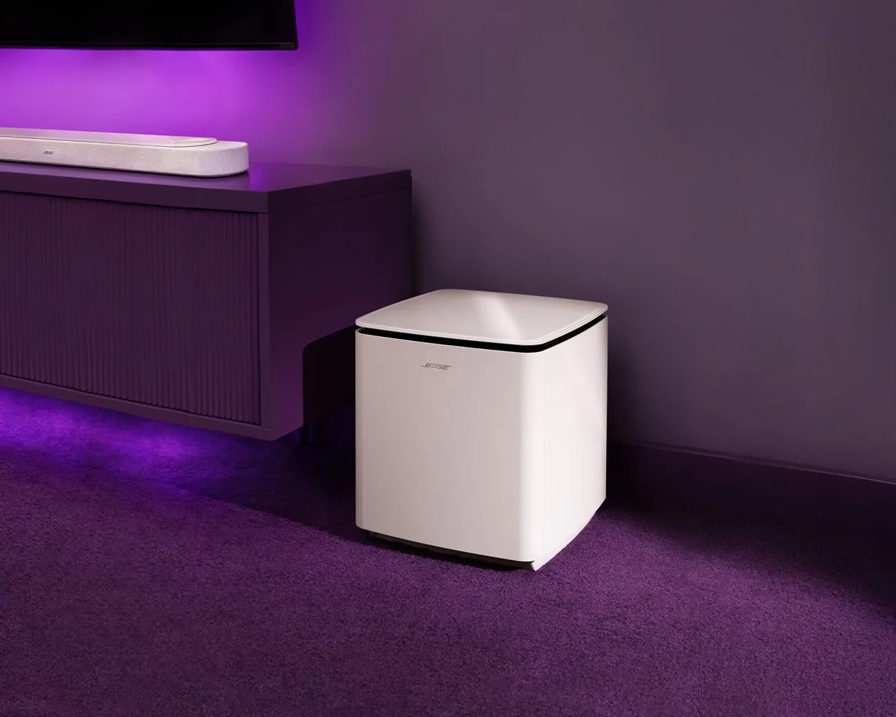 White Bose subwoofer speaker on purple carpet next to a purple media console with a white soundbar on top.