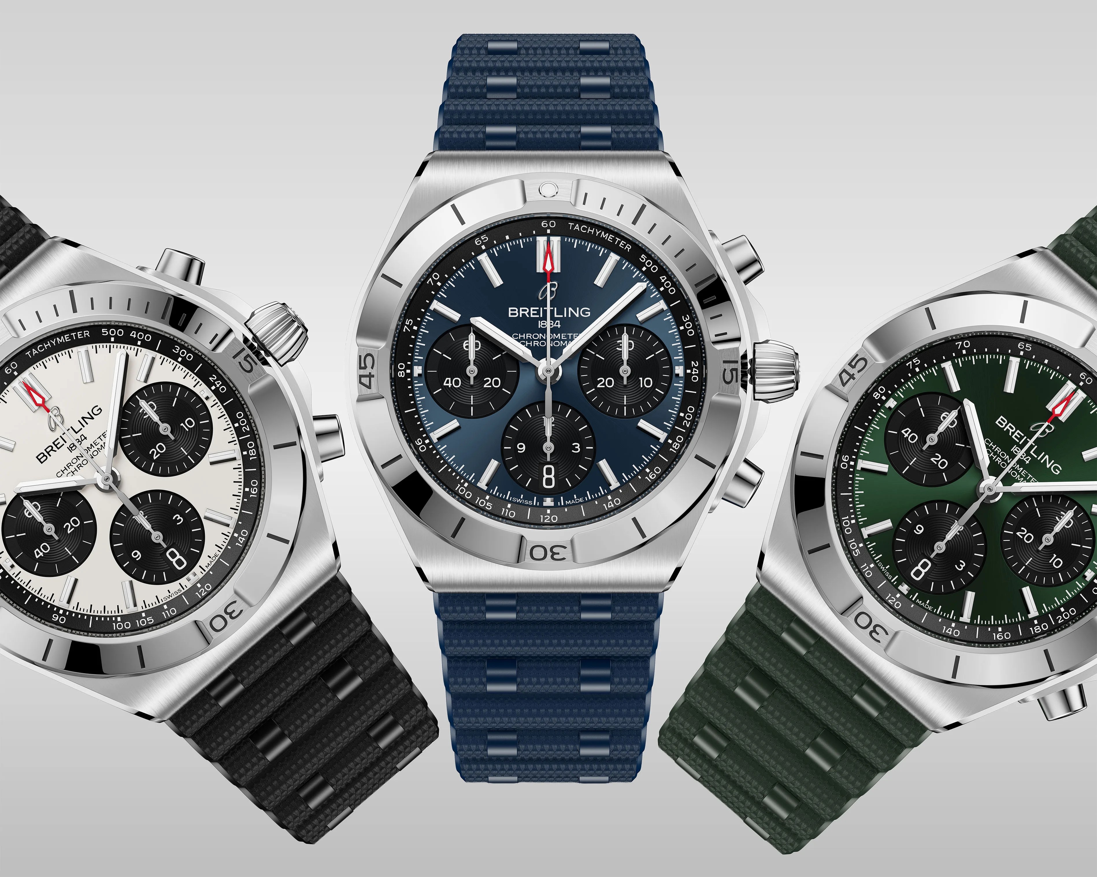 Three Breitling chronograph watches with stainless steel cases and textured rubber straps in black, blue, and green, featuring tachymeter bezels and subdials.