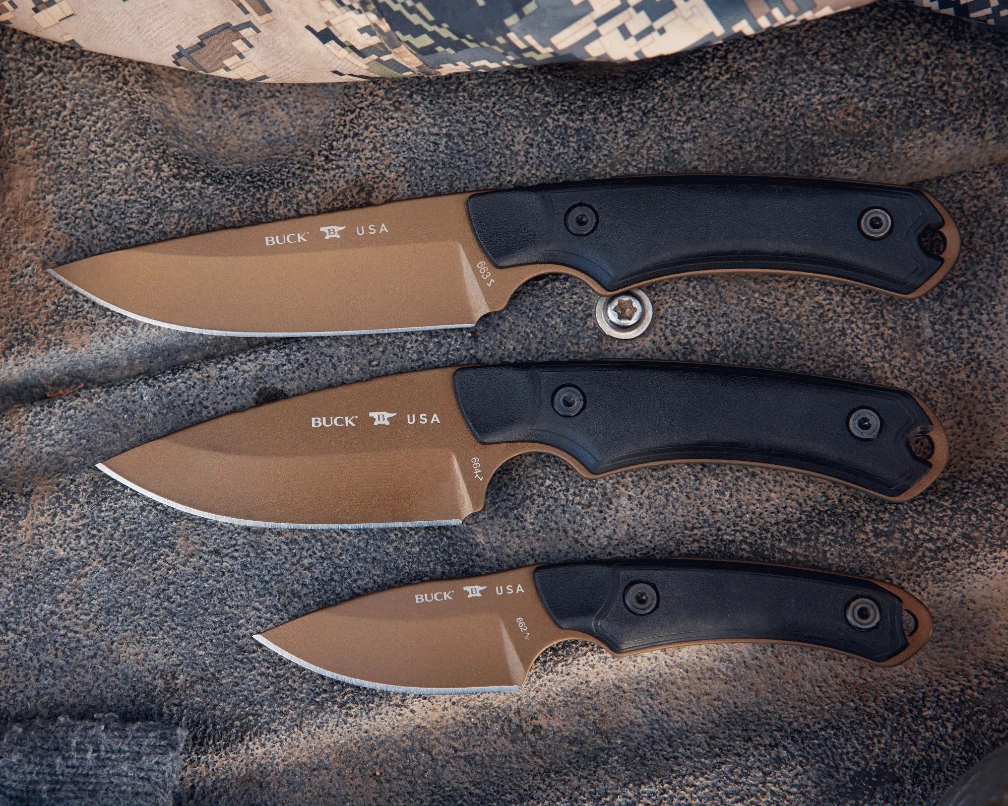 Three Buck USA fixed-blade knives with tan blades and black handles laid on a textured surface.