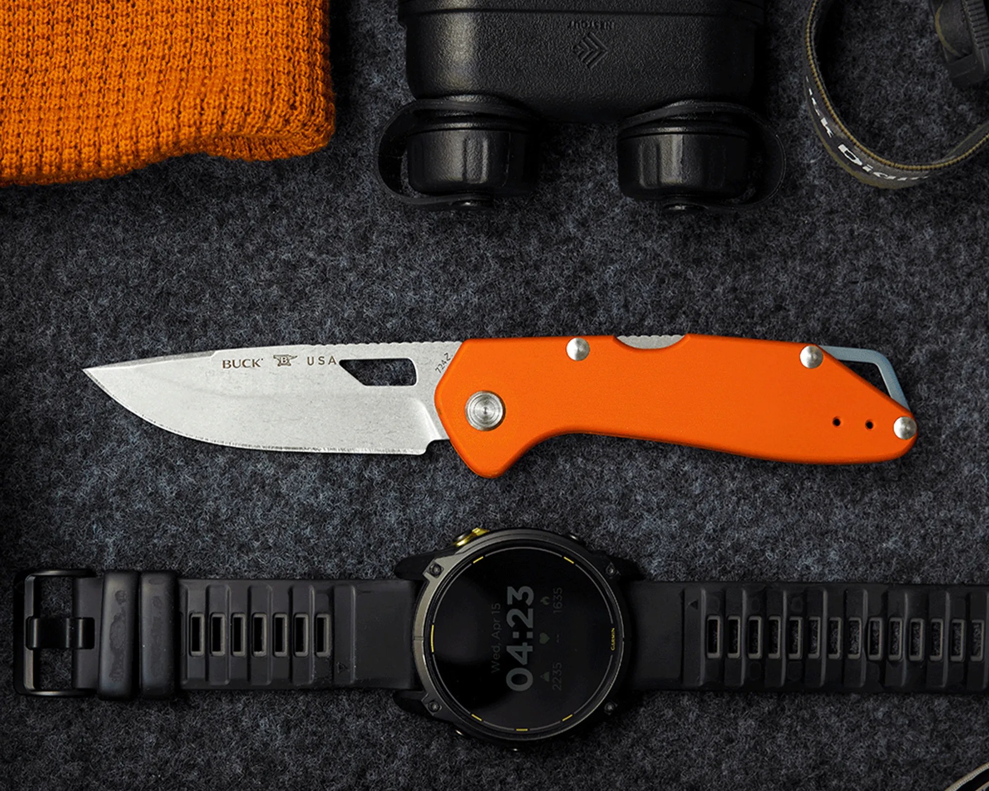 Orange-handled Buck folding knife with a partially serrated stainless steel blade on a dark textured surface.