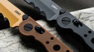 Two CRKT folding knives with serrated blades, one with a tan handle and blade, the other with a black handle and blade, on a map.