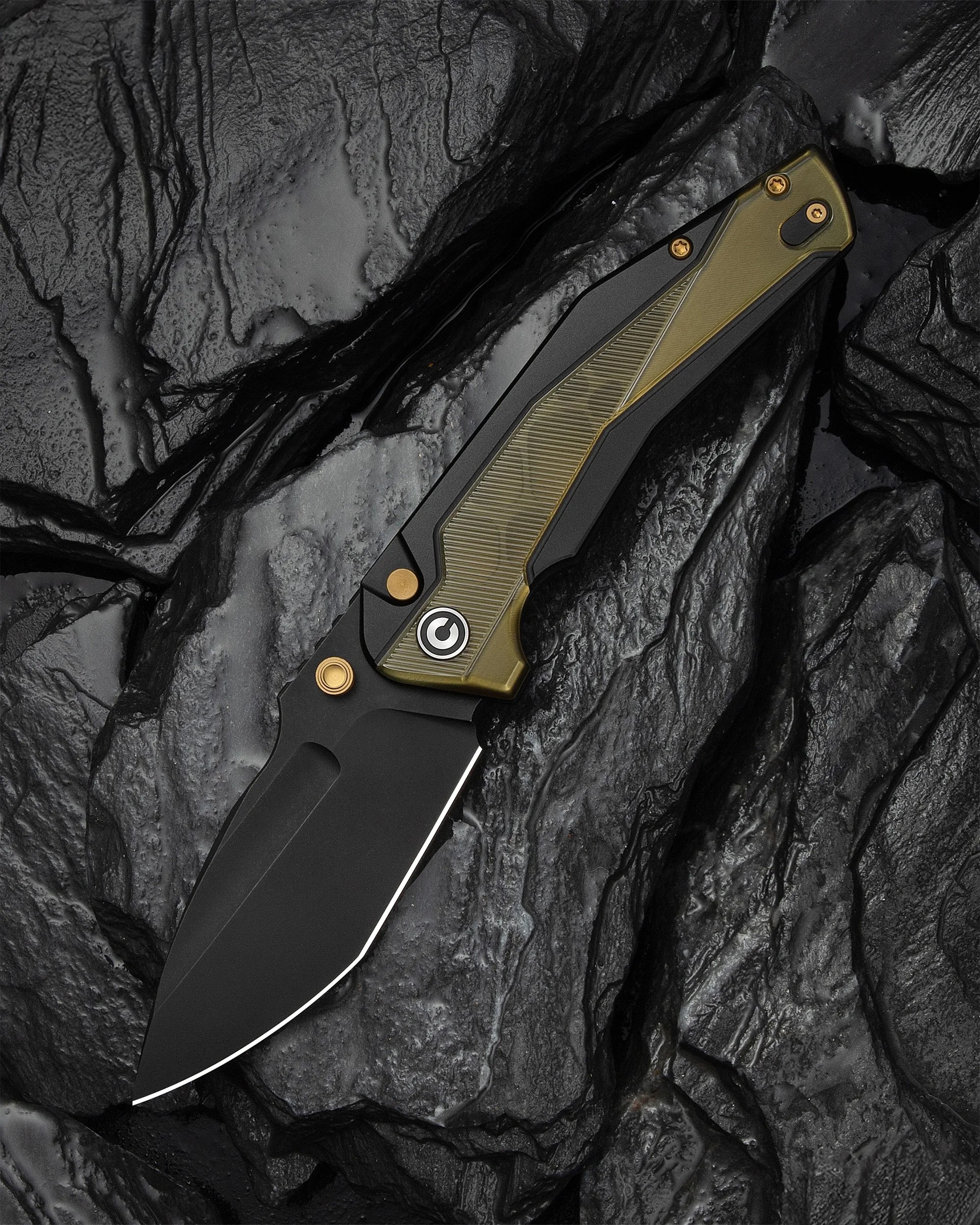 Black folding knife with olive green and black textured handle on dark textured rocks.