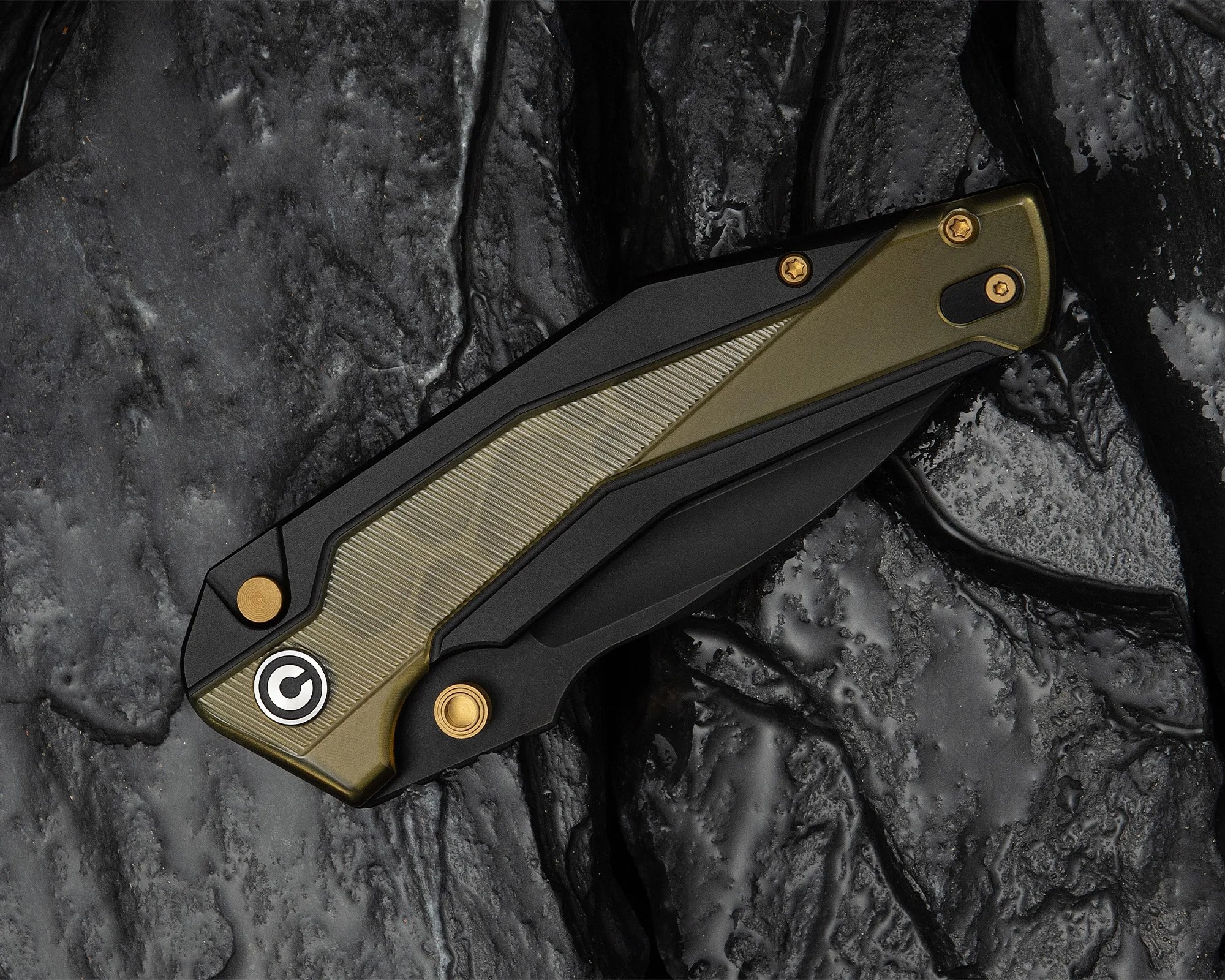 Folded black and olive green pocket knife with gold screws on a textured dark stone surface.