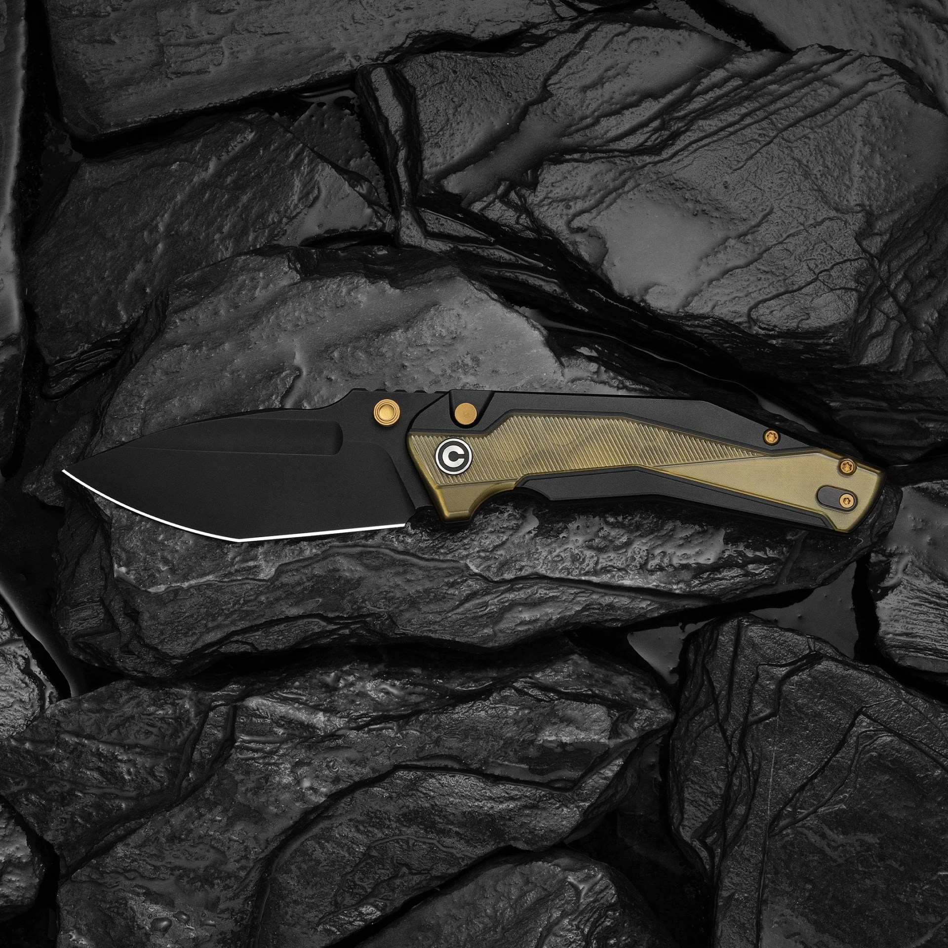 Black folding knife with gold screws and textured olive green handle on dark stone surface.