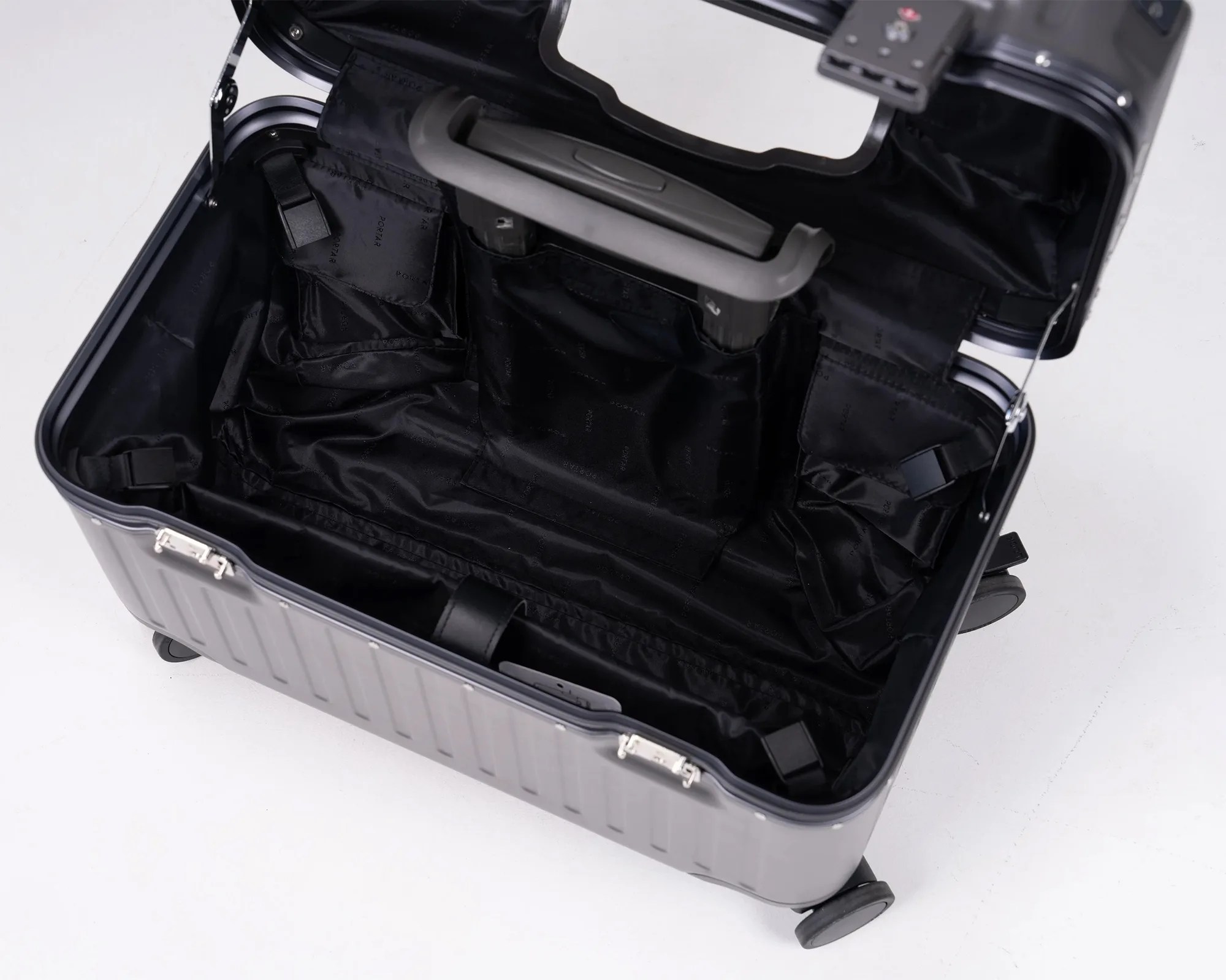Open black hard-shell suitcase with black fabric interior lining and a gray handle inside.