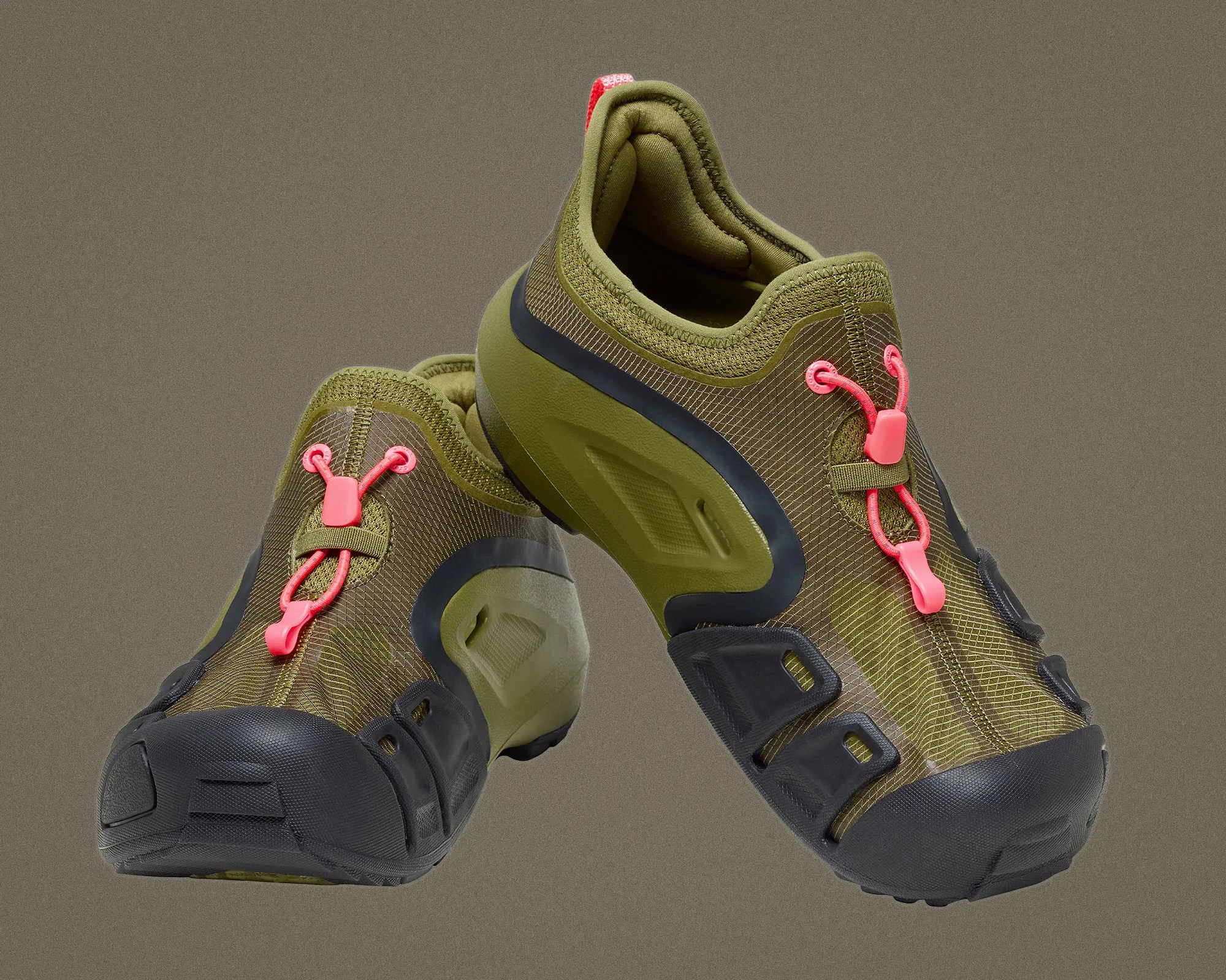 Pair of olive green athletic shoes with black soles and bright pink lace locks on a gray background.