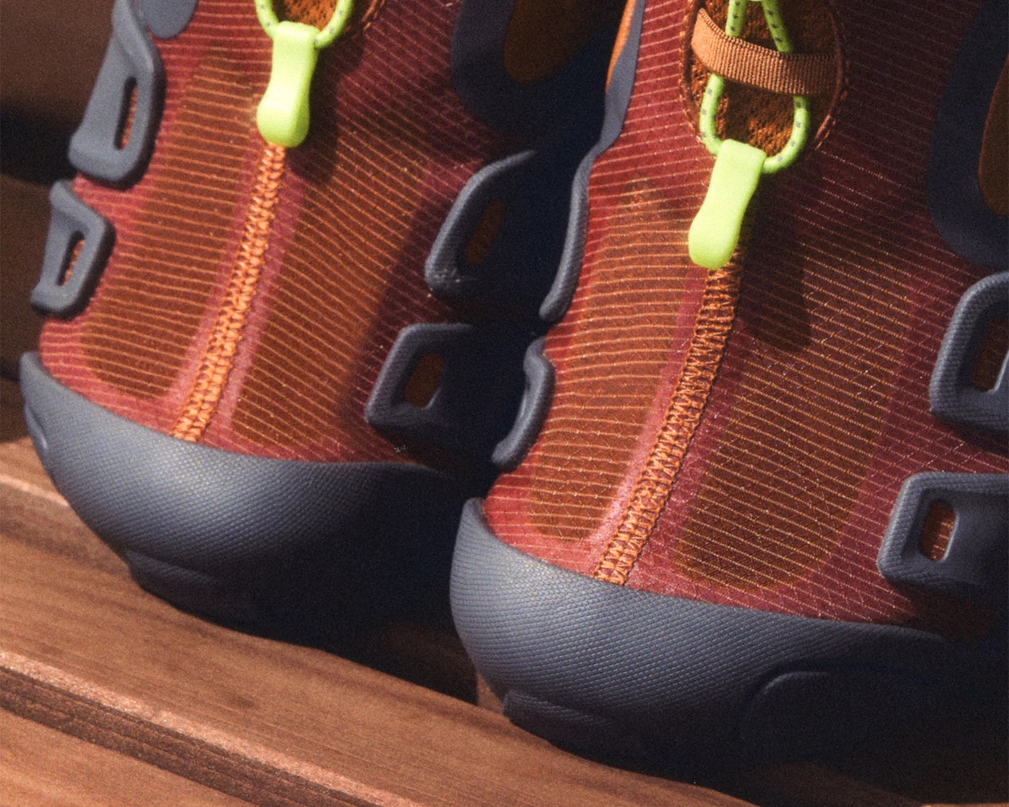 Close-up of brown and orange shoes with neon green lace loops and gray soles on a wooden surface.