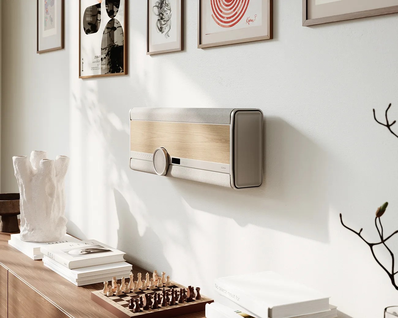 Wall-mounted beige and wood-finish speaker with a large circular knob in a bright room above a wooden cabinet with books and a chessboard.
