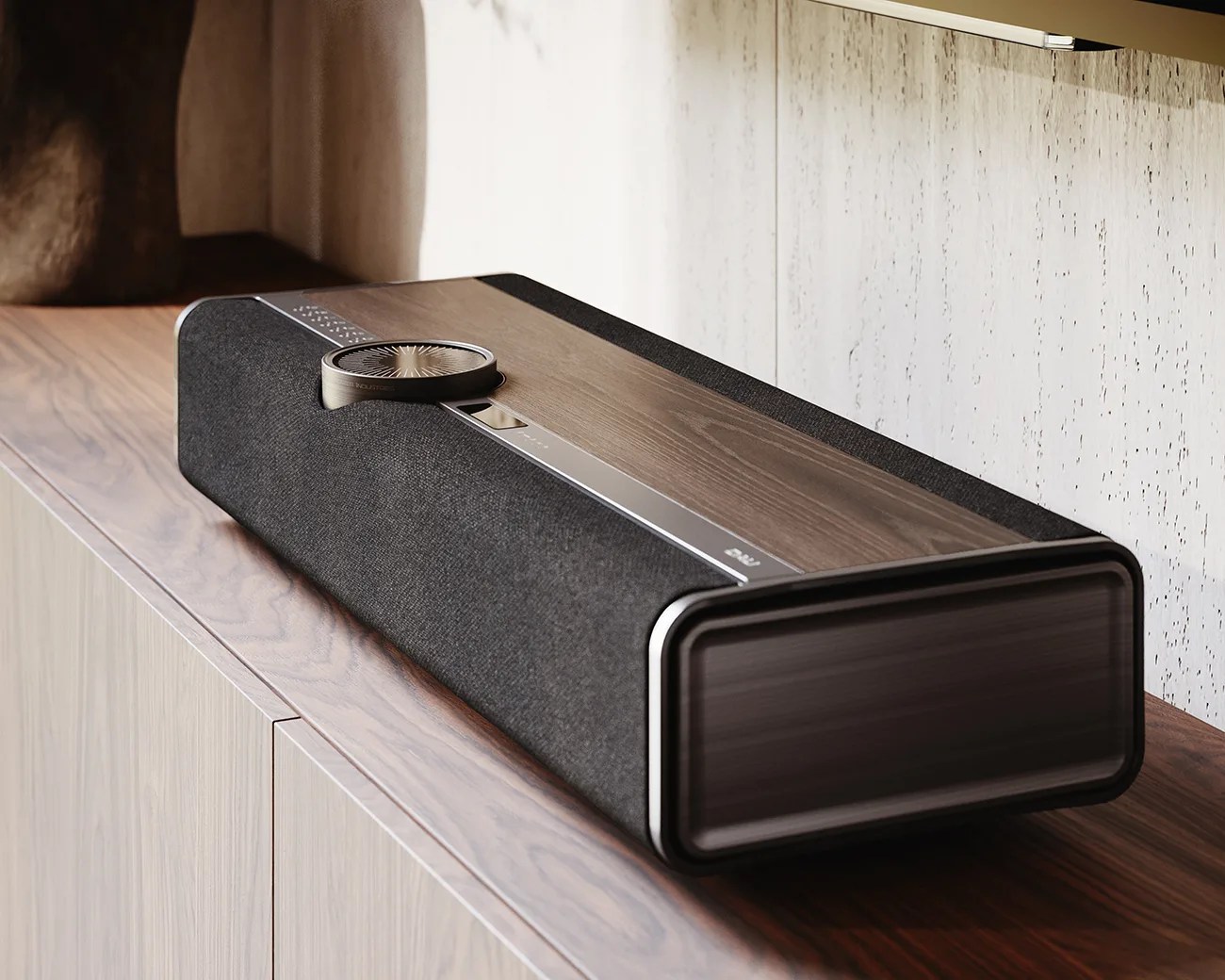 Rectangular black fabric and wood-finish soundbar with a large circular dial on top, placed on a wooden cabinet.