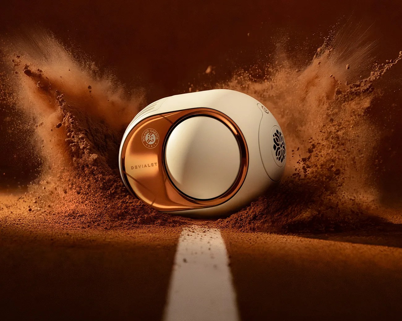 White and copper Devialet speaker with Roland Garros logo on a clay tennis court with dust flying.
