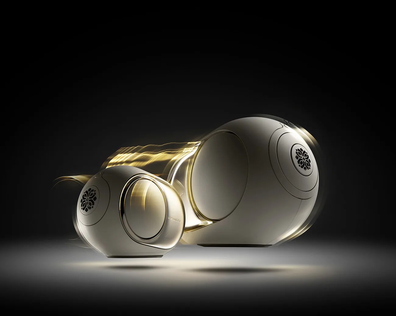 Pair of sleek, white spherical speakers with black grille and gold light trails on a dark background.